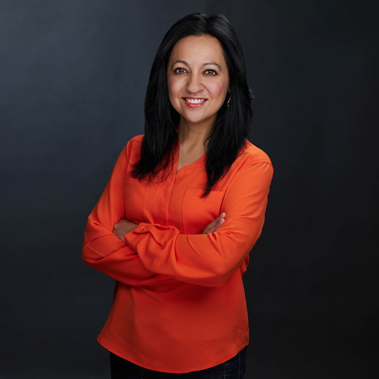 Corporate headshot of a woman in an orange blouse on a dark background