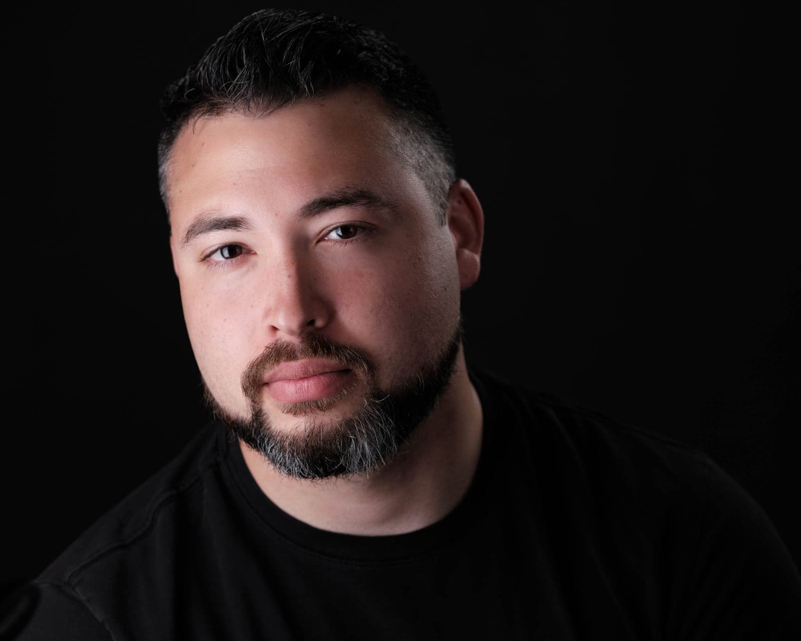 Dramatic headshot of a bearded man in black on a dark background