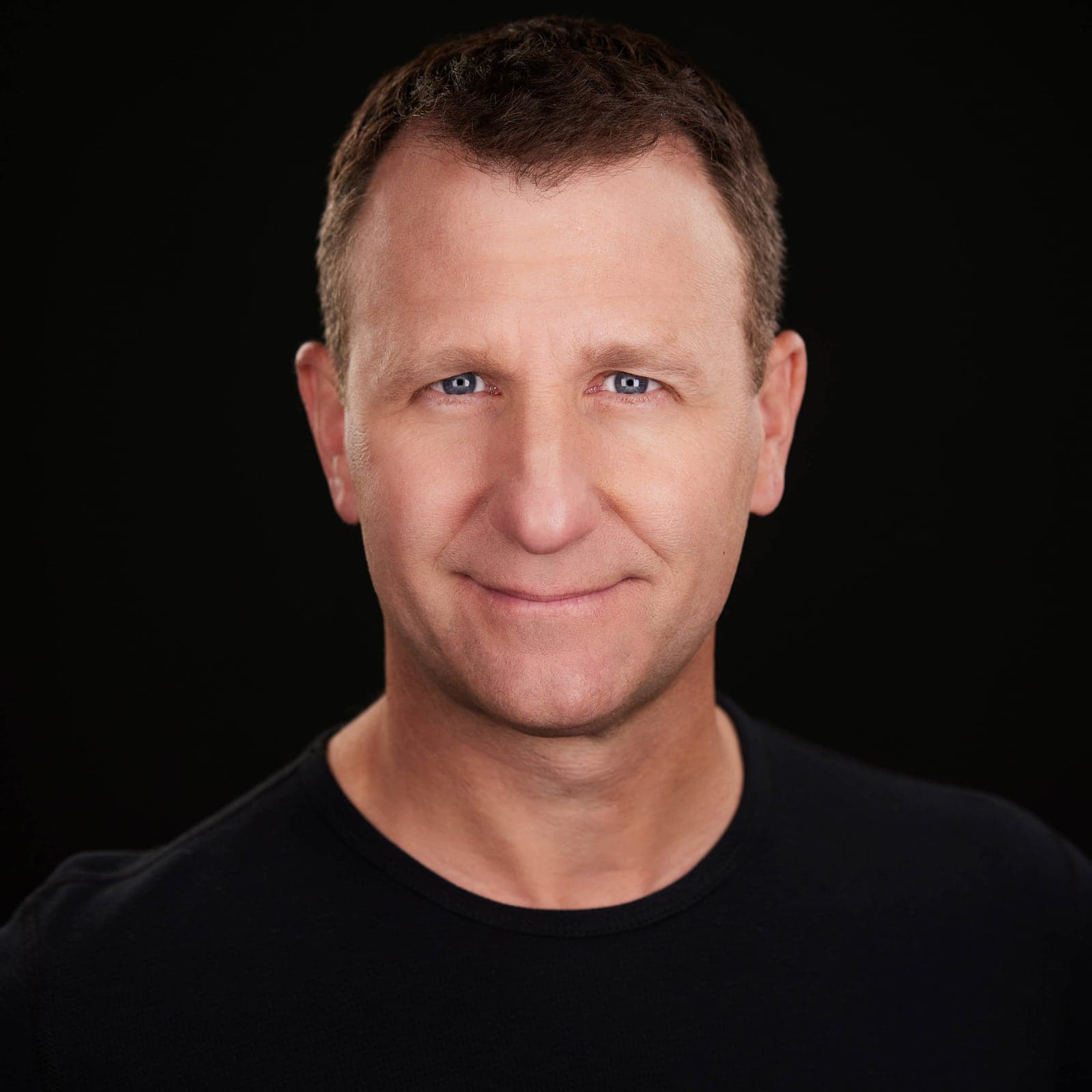 Professional headshot of a man in a black polo on a black background