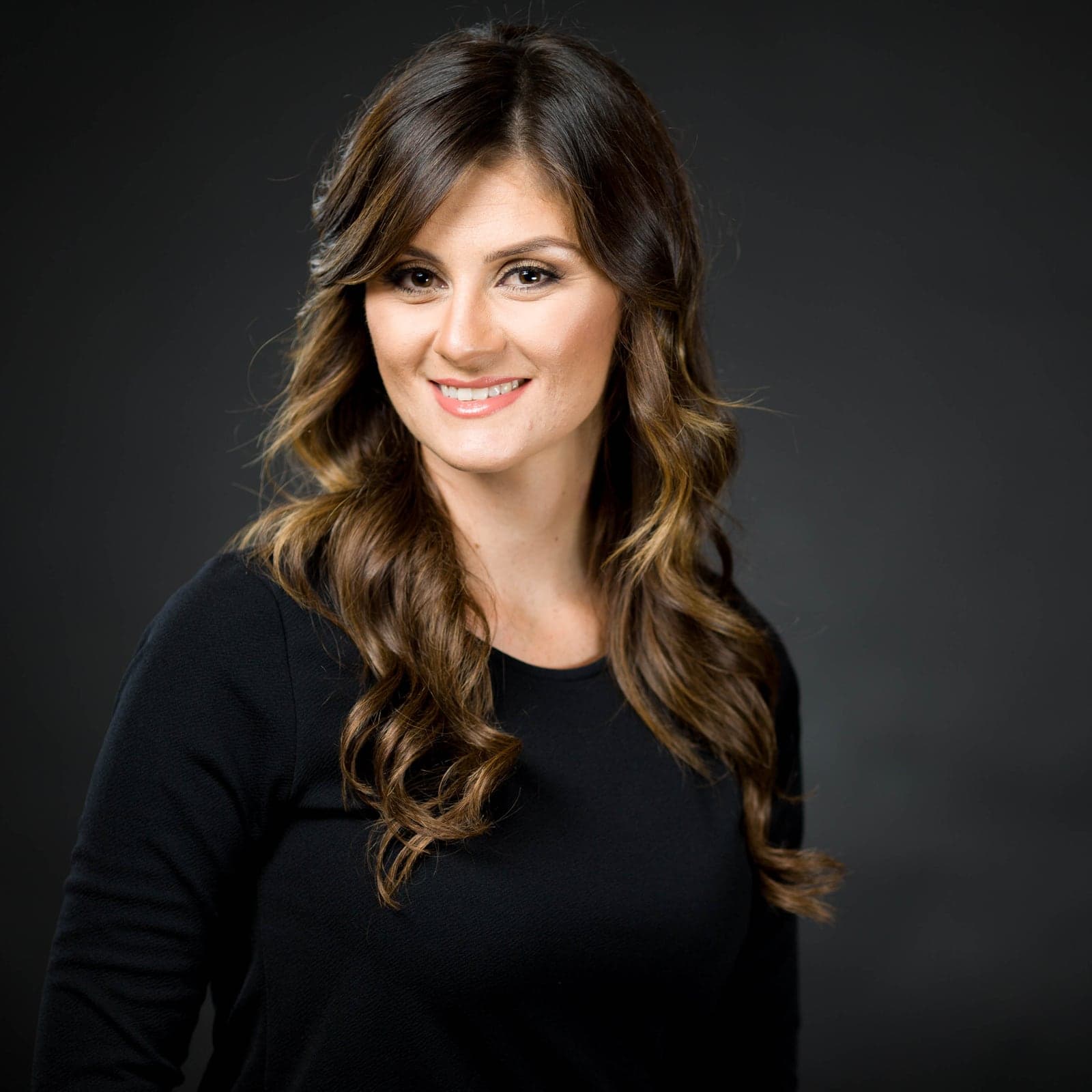 Professional headshot of a woman with wavy hair on a dark background