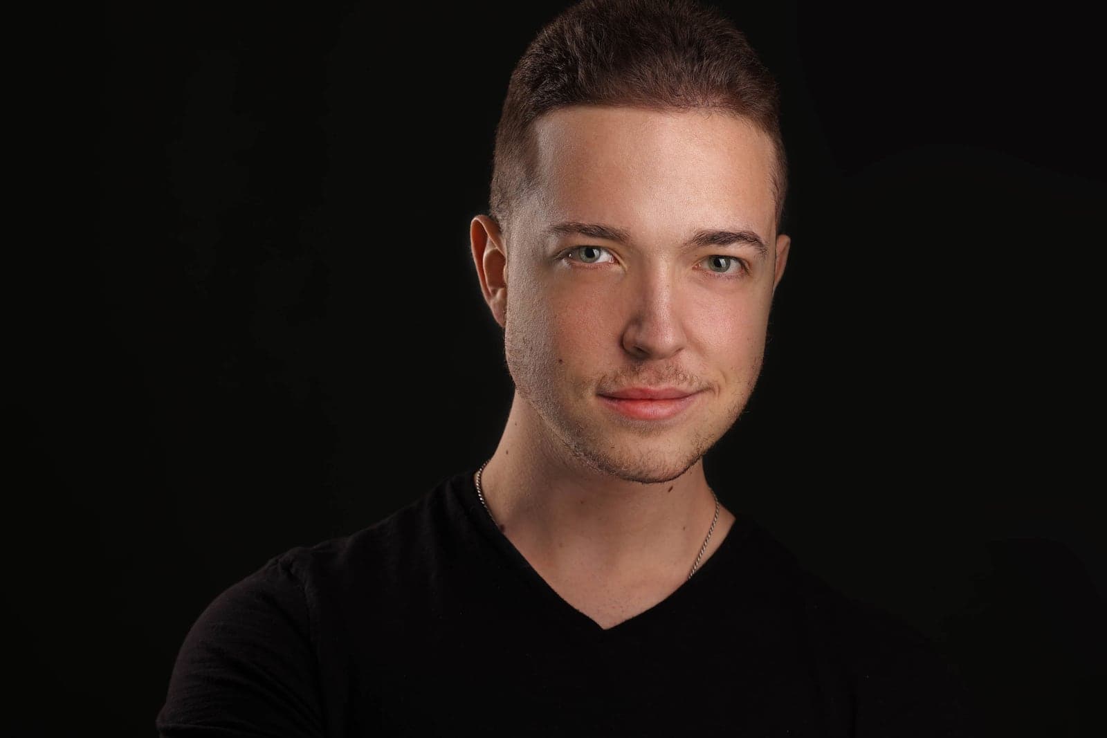 Professional headshot of a young man in a black v-neck on a dark background