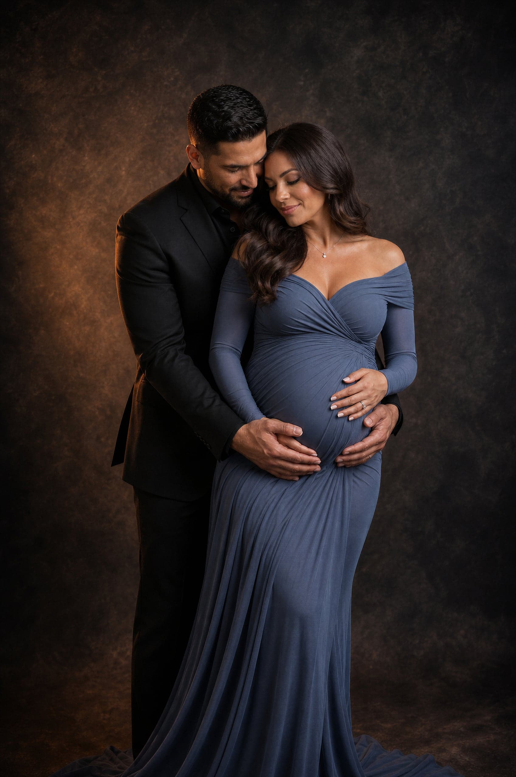 Expecting couple in an intimate studio portrait, mother in dusty blue