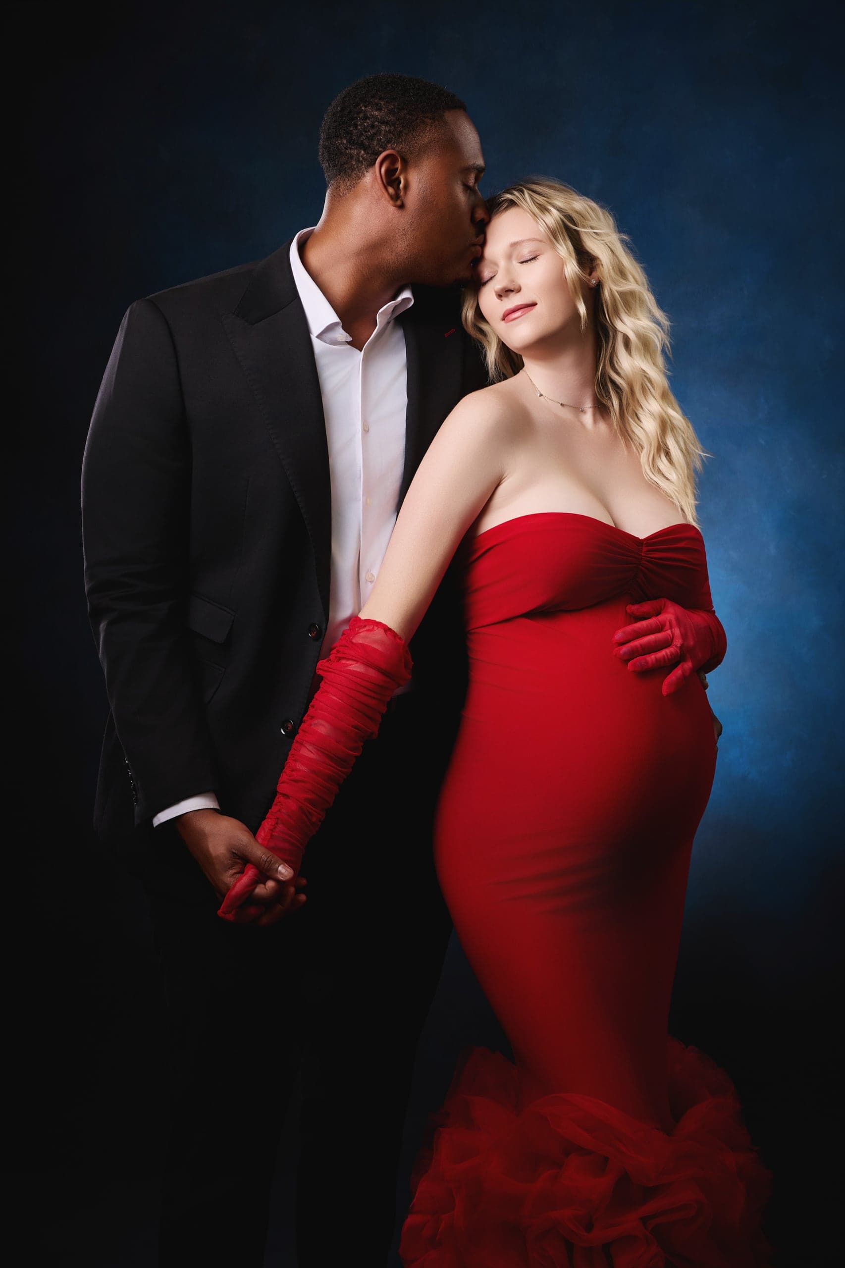Expecting couple in a formal maternity portrait, mother in red