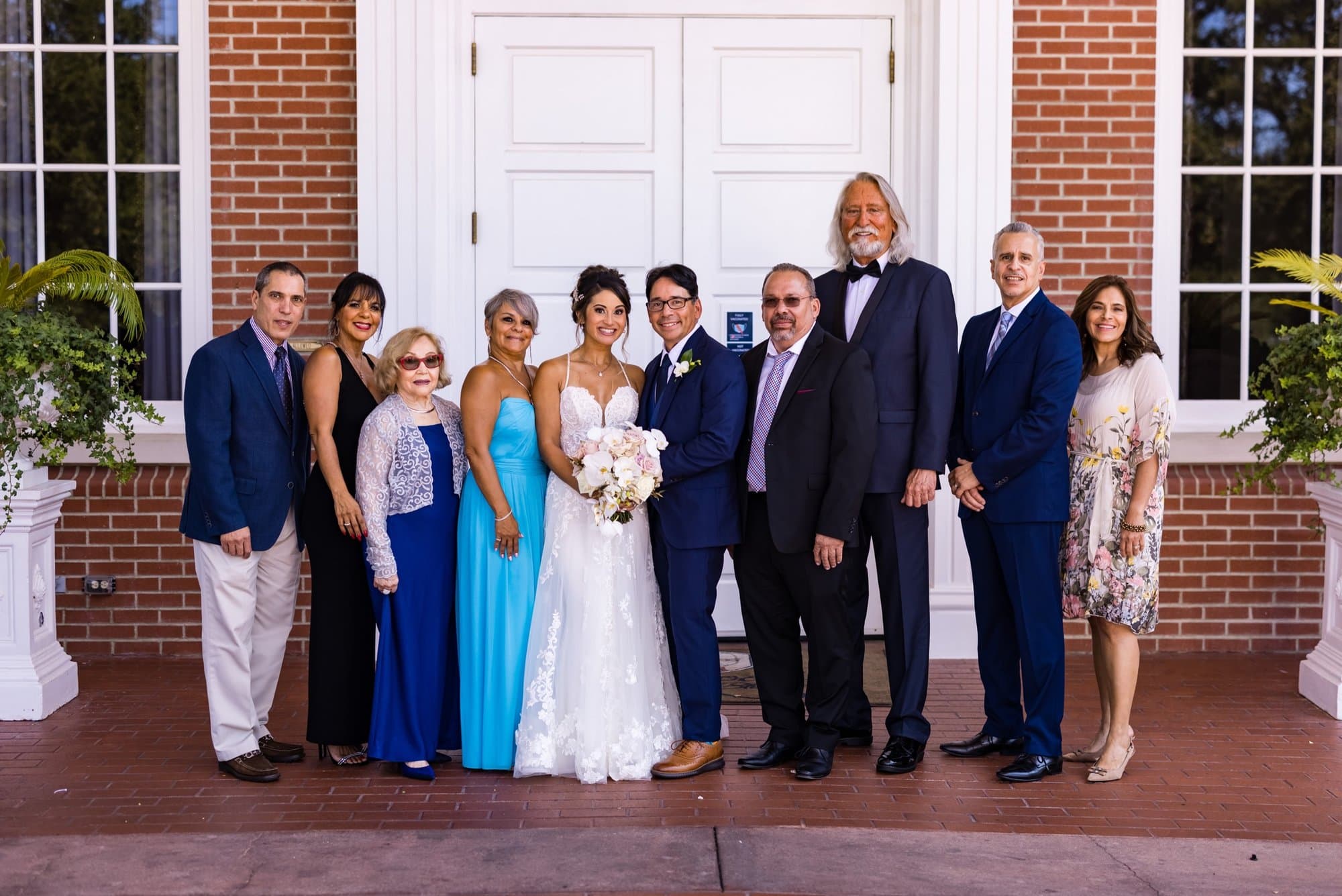 An extended family formal with the bride and groom centered before the white doors of a country club