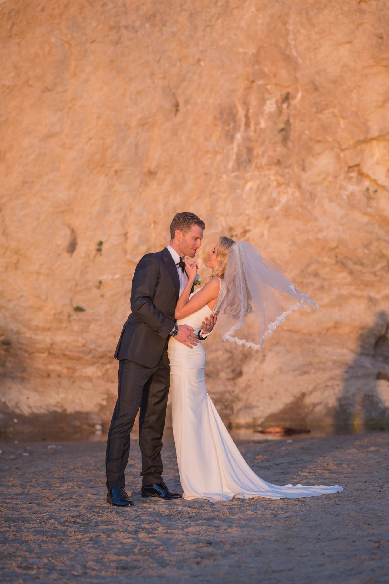 The newlyweds sharing a portrait against coastal sandstone