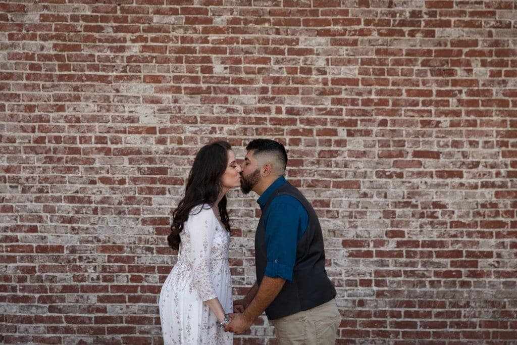 Early-morning couples portrait in a string-lit brick alley in Old Town Pasadena, with historic storefronts behind.