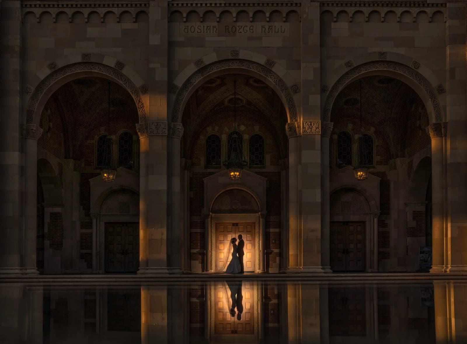 A couple on the wide brick Janss Steps at UCLA in Westwood, with the Romanesque towers of Royce Hall behind them in early morning light.