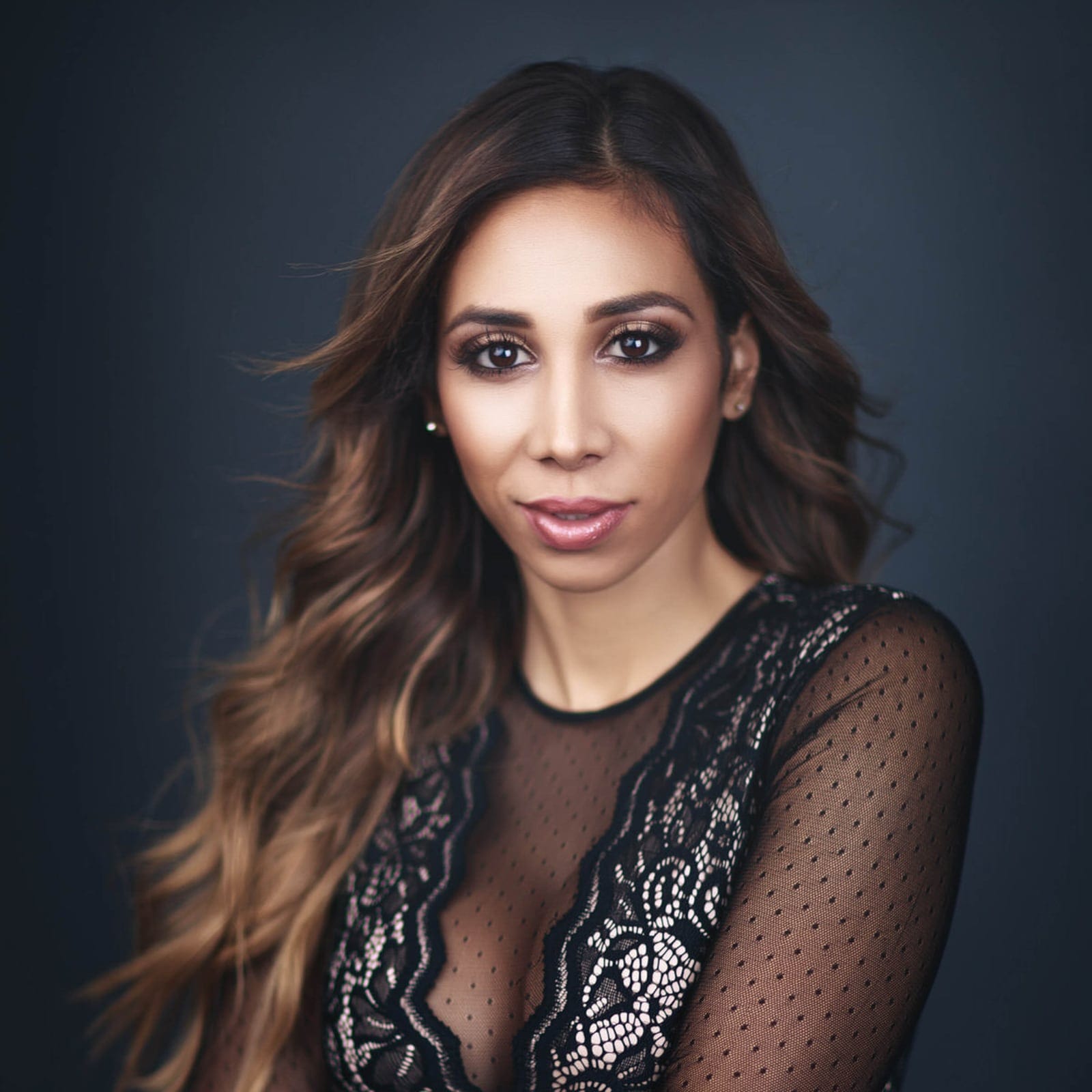 Editorial branding headshot of a woman in a black lace top on a navy background