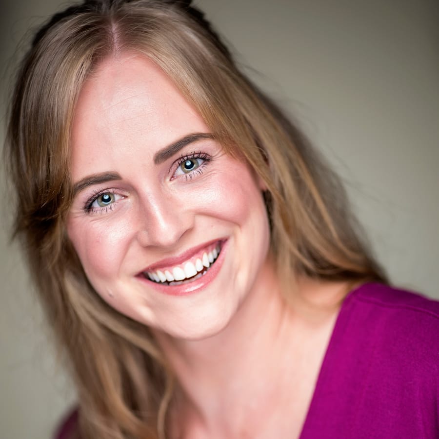Professional headshot of a woman in magenta on a dark backdrop