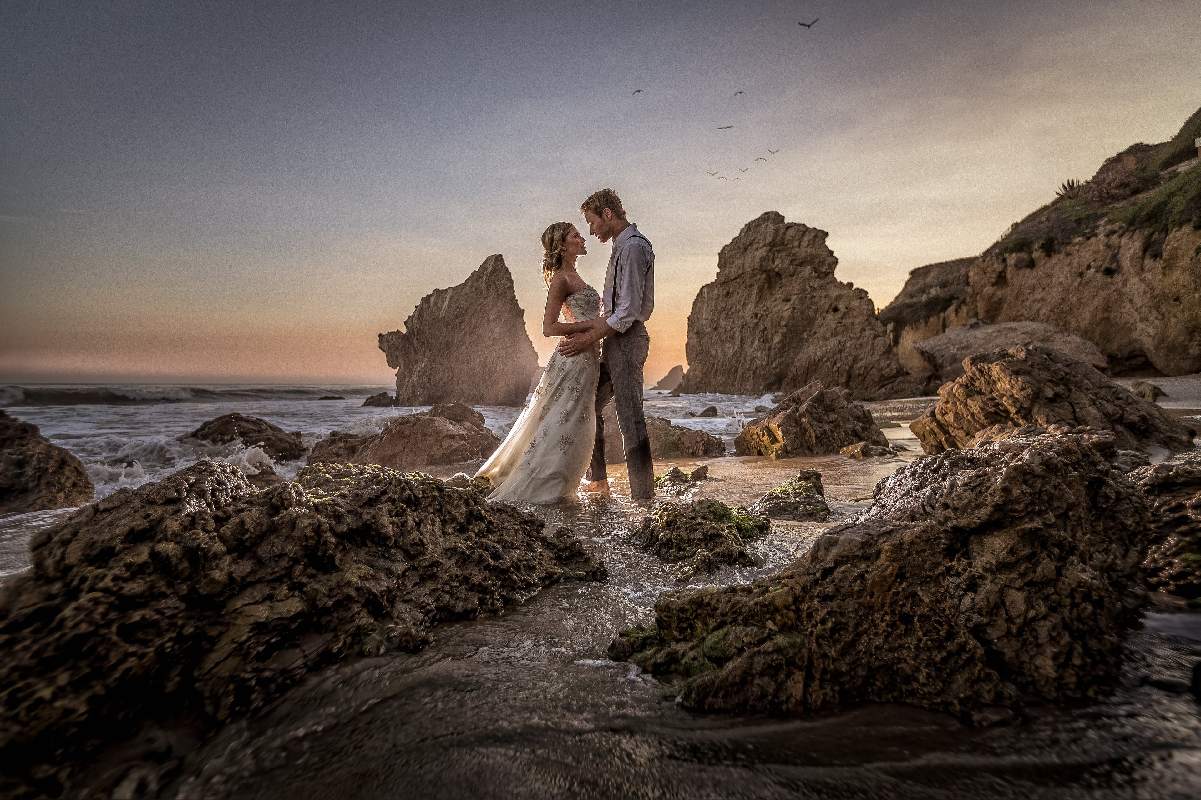 Newlyweds standing among the rocks at El Matador Beach at sunset