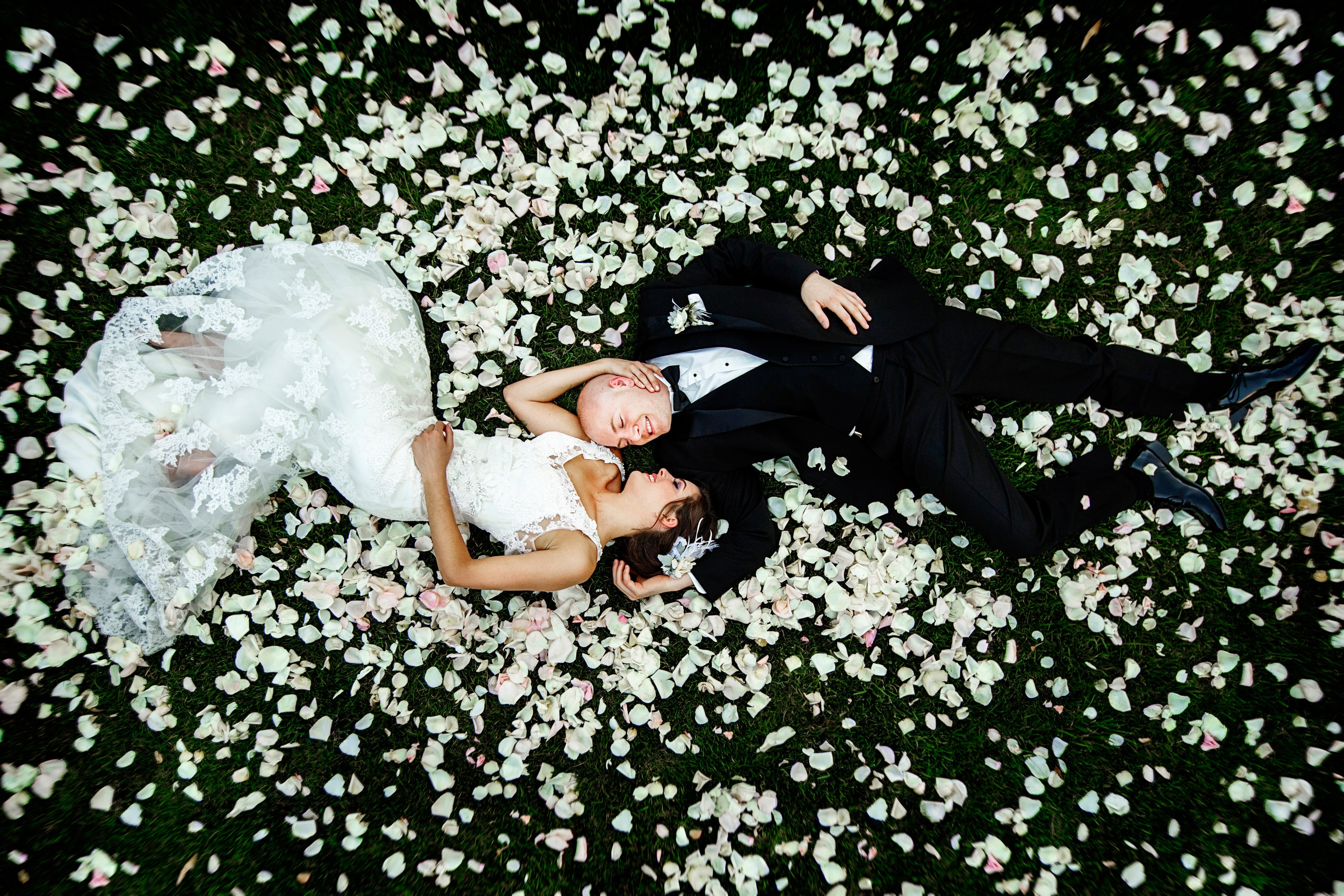 Newlyweds lying together among white rose petals