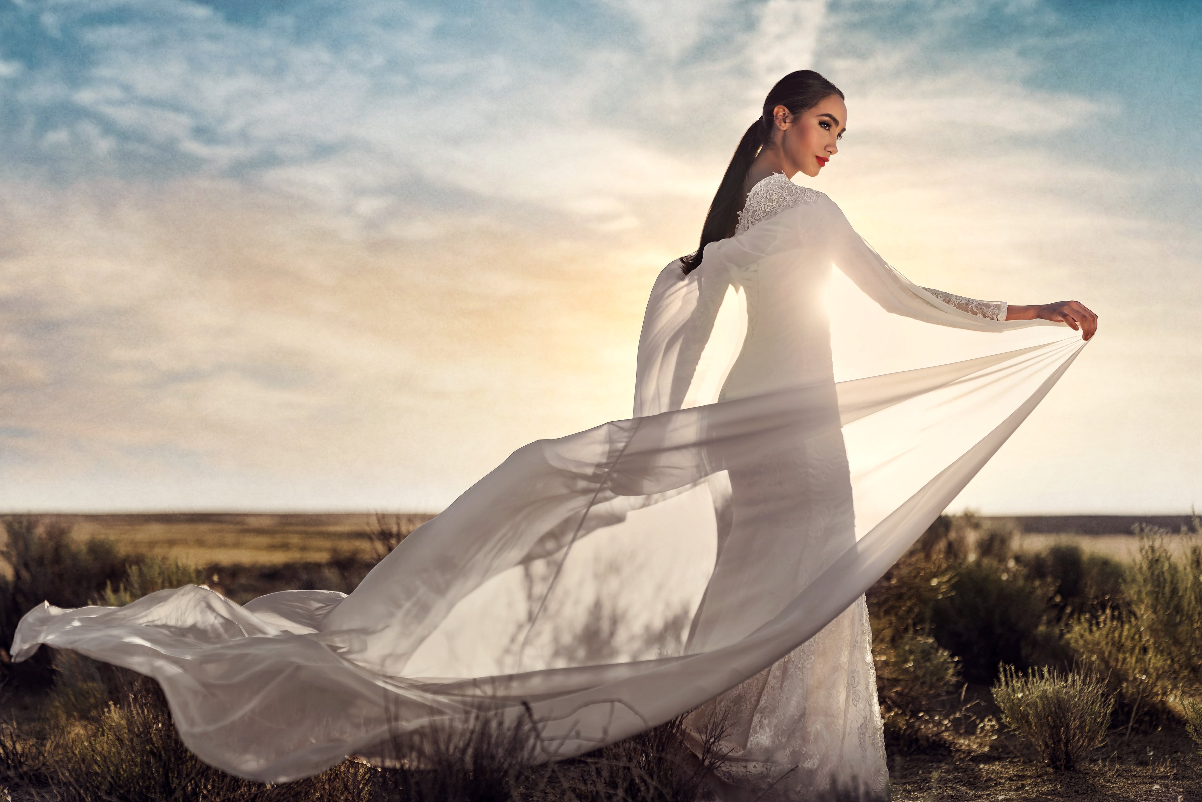 Bride holding her flowing gown in a windswept landscape