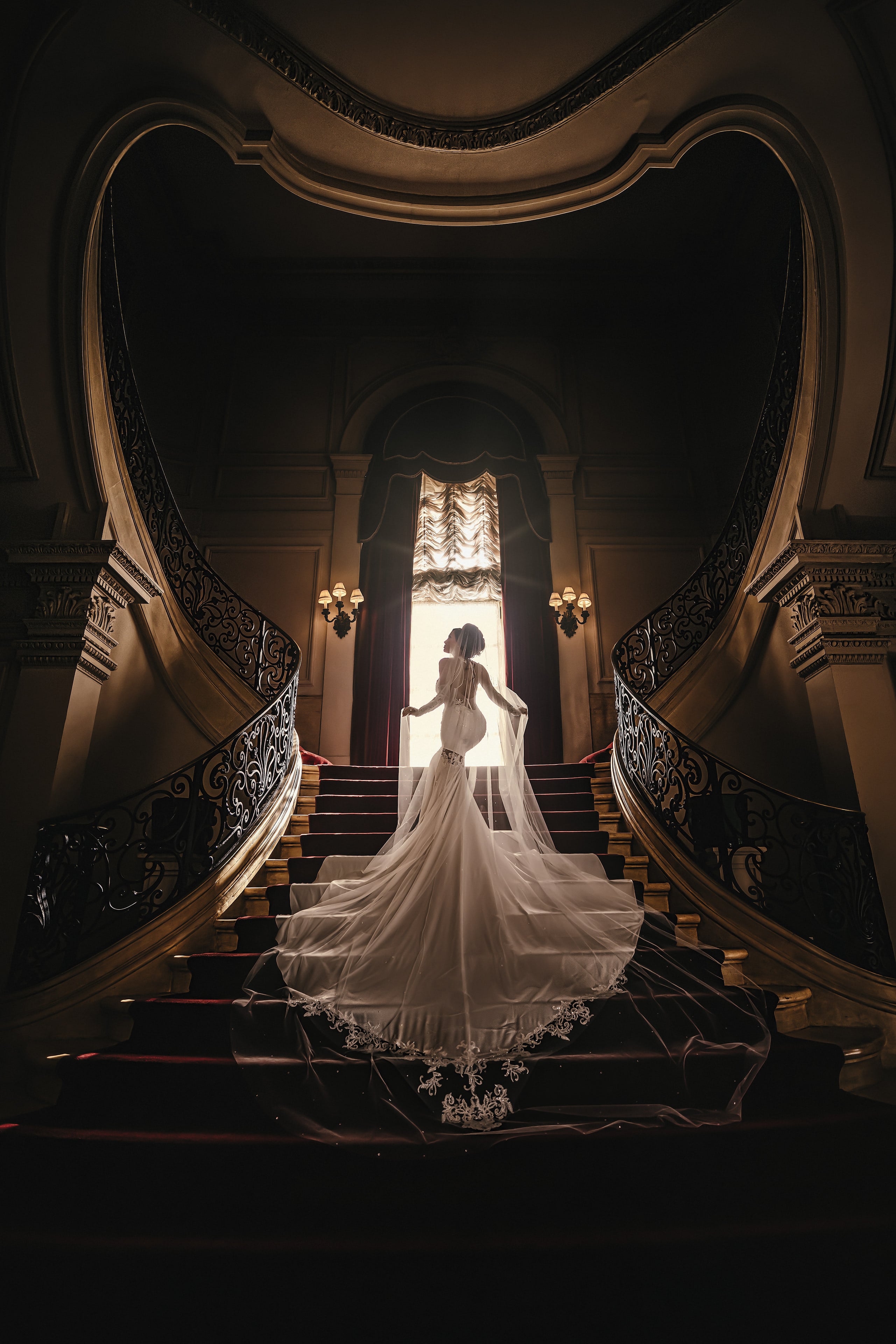 Bride and groom framed by a sculptural staircase and trailing veil