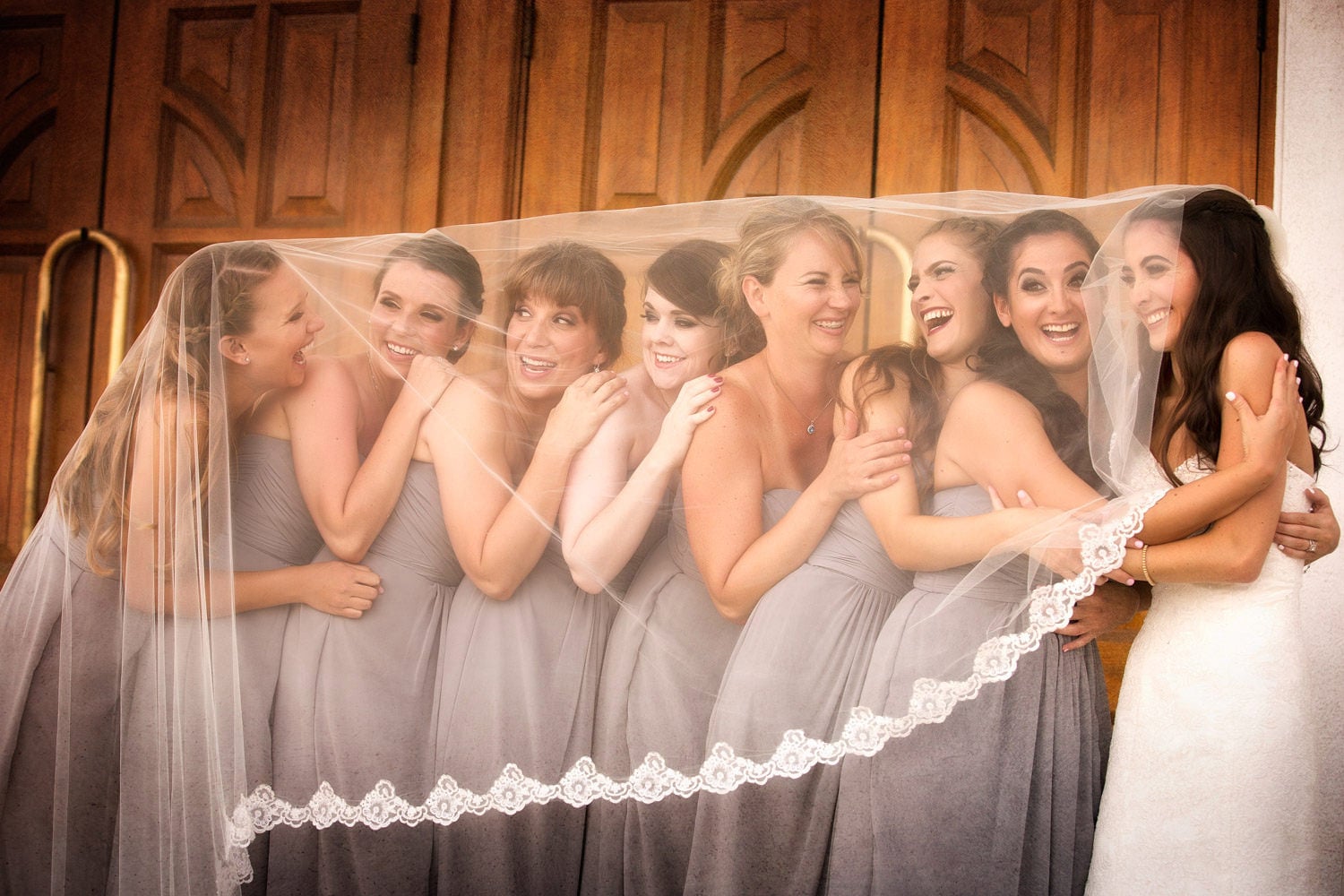 Bride and bridesmaids sharing a playful moment beneath a lace veil