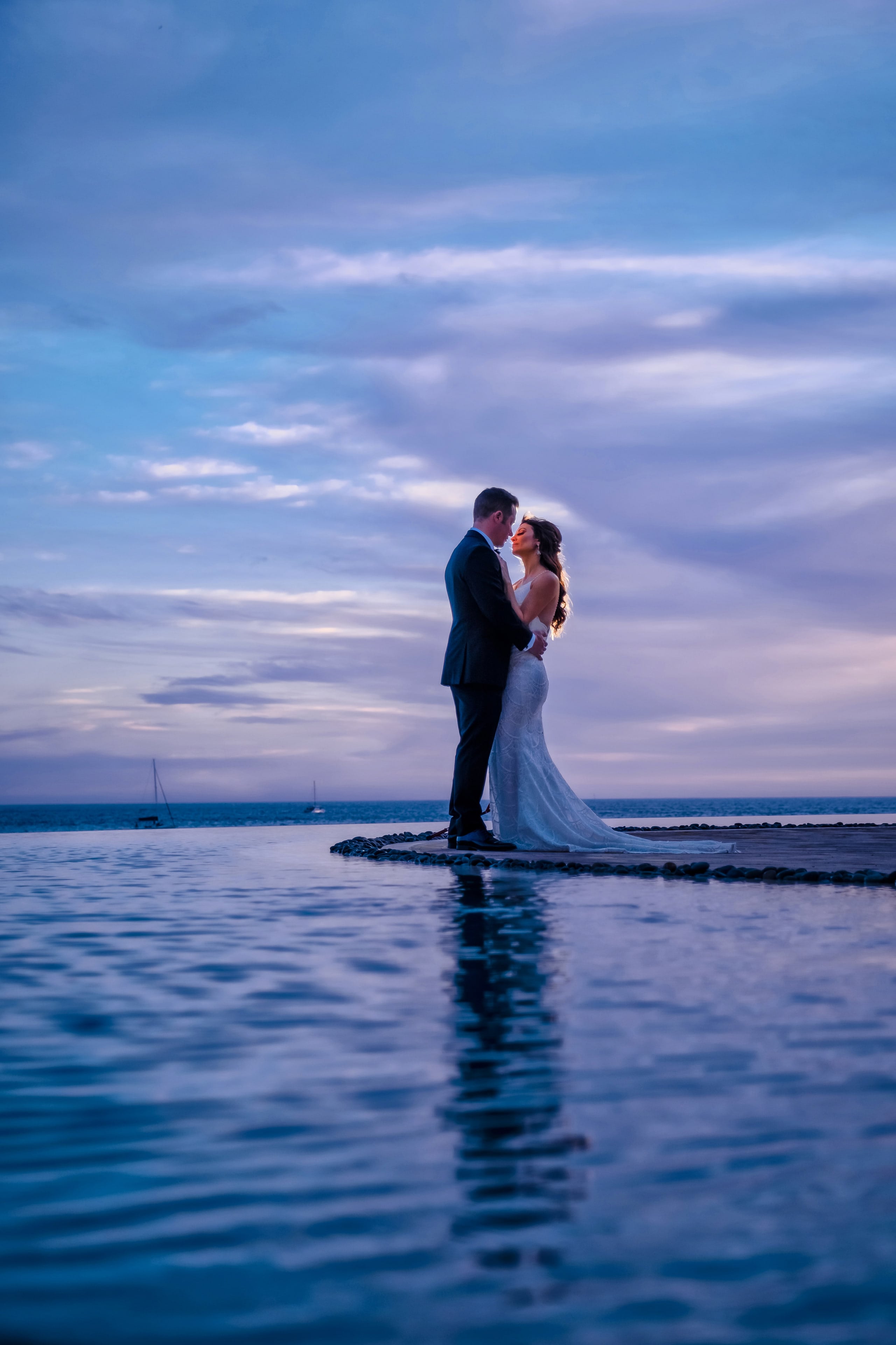 Newlyweds reflected in a pool beneath a blue Cabo sky