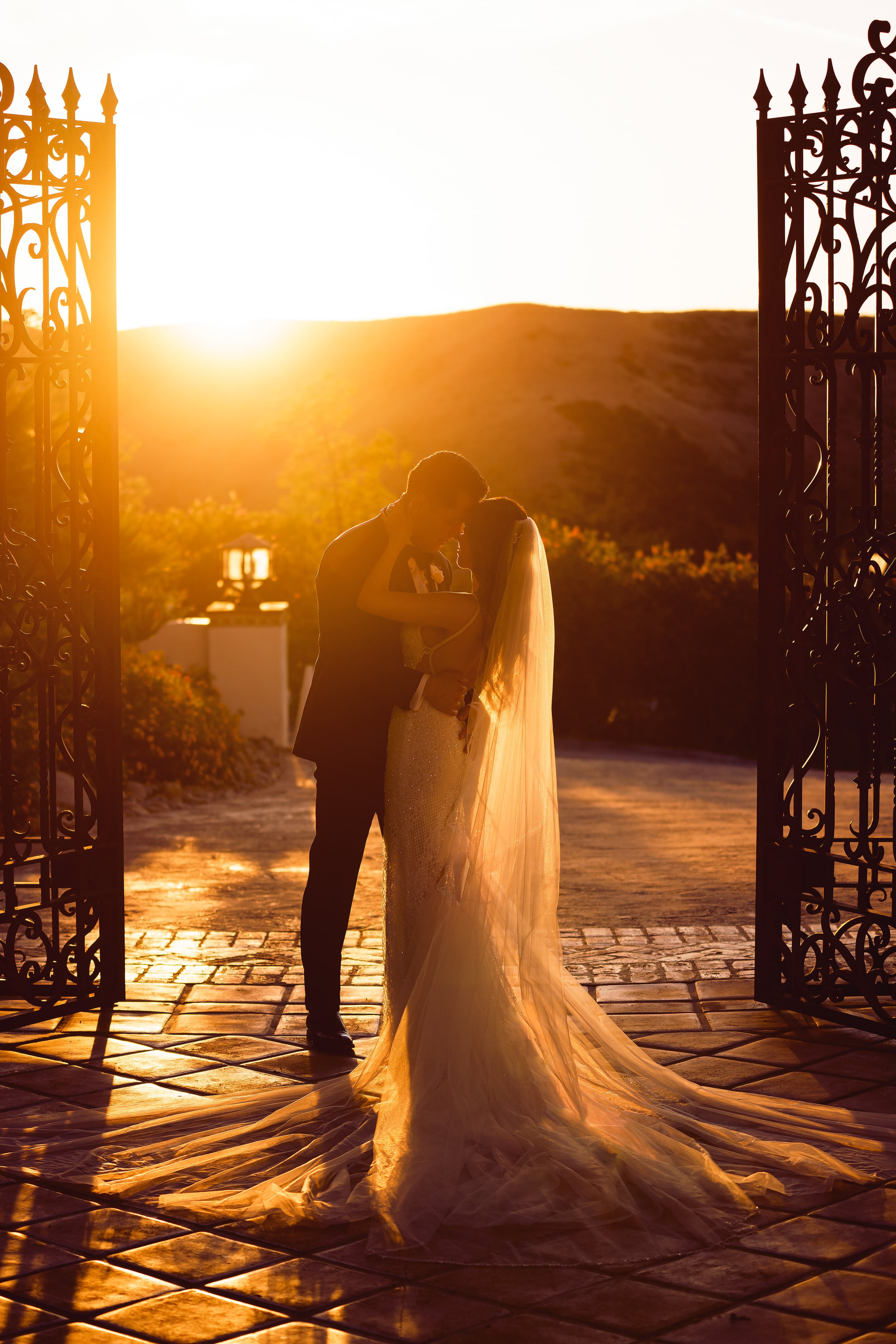 Newlyweds silhouetted at sunset between ornate villa gates