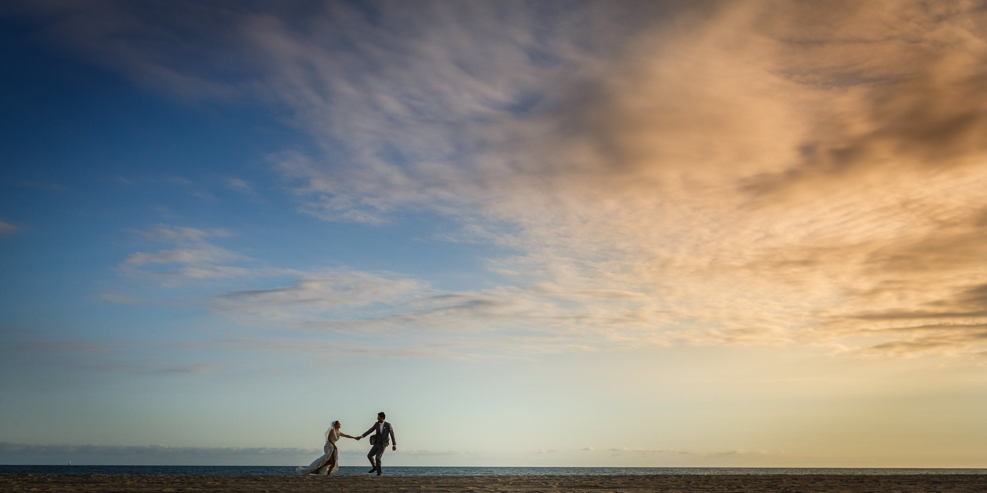 Newlyweds walking beneath an expansive pastel evening sky