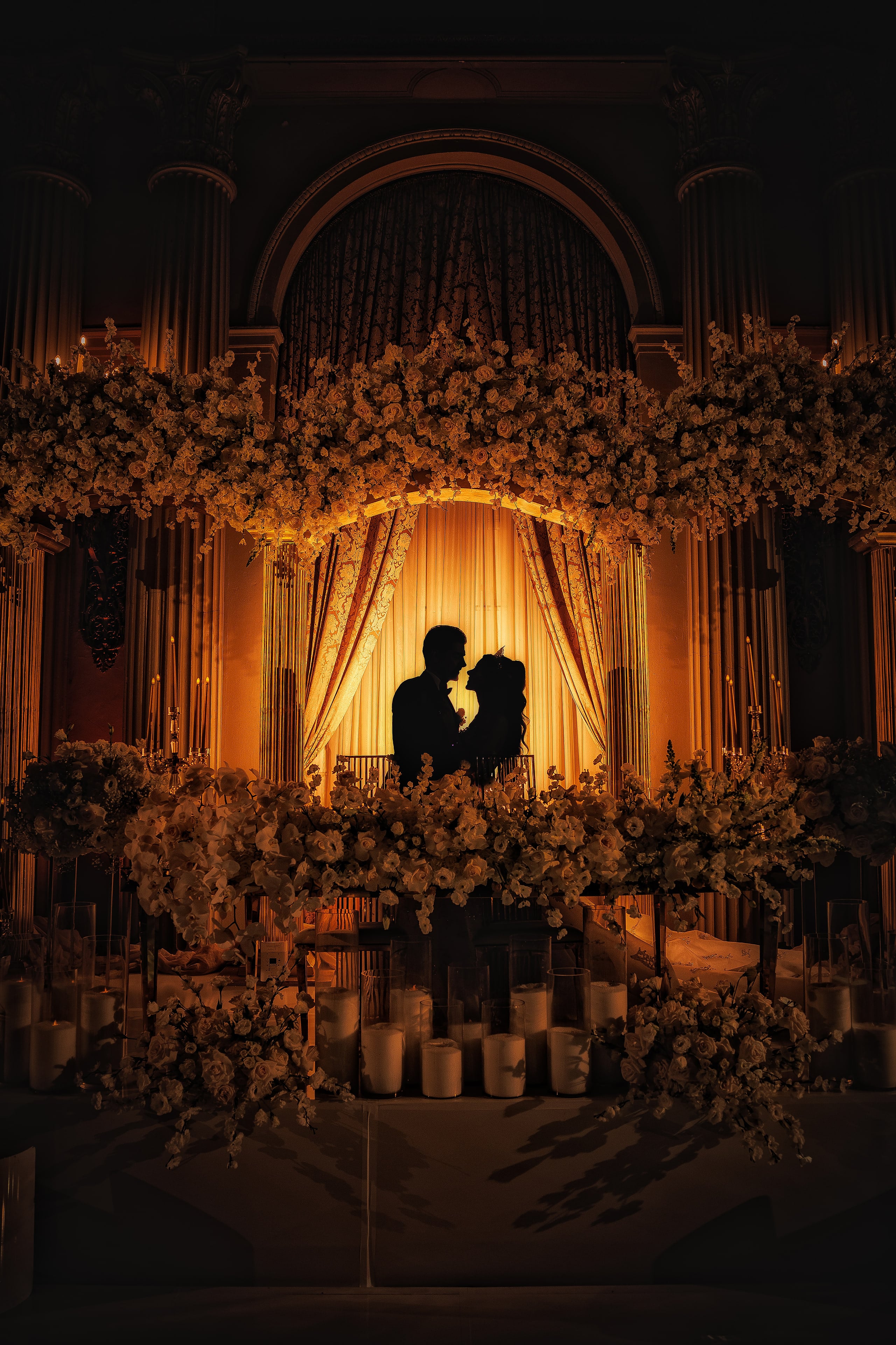 Newlyweds silhouetted beneath an illuminated ballroom arch