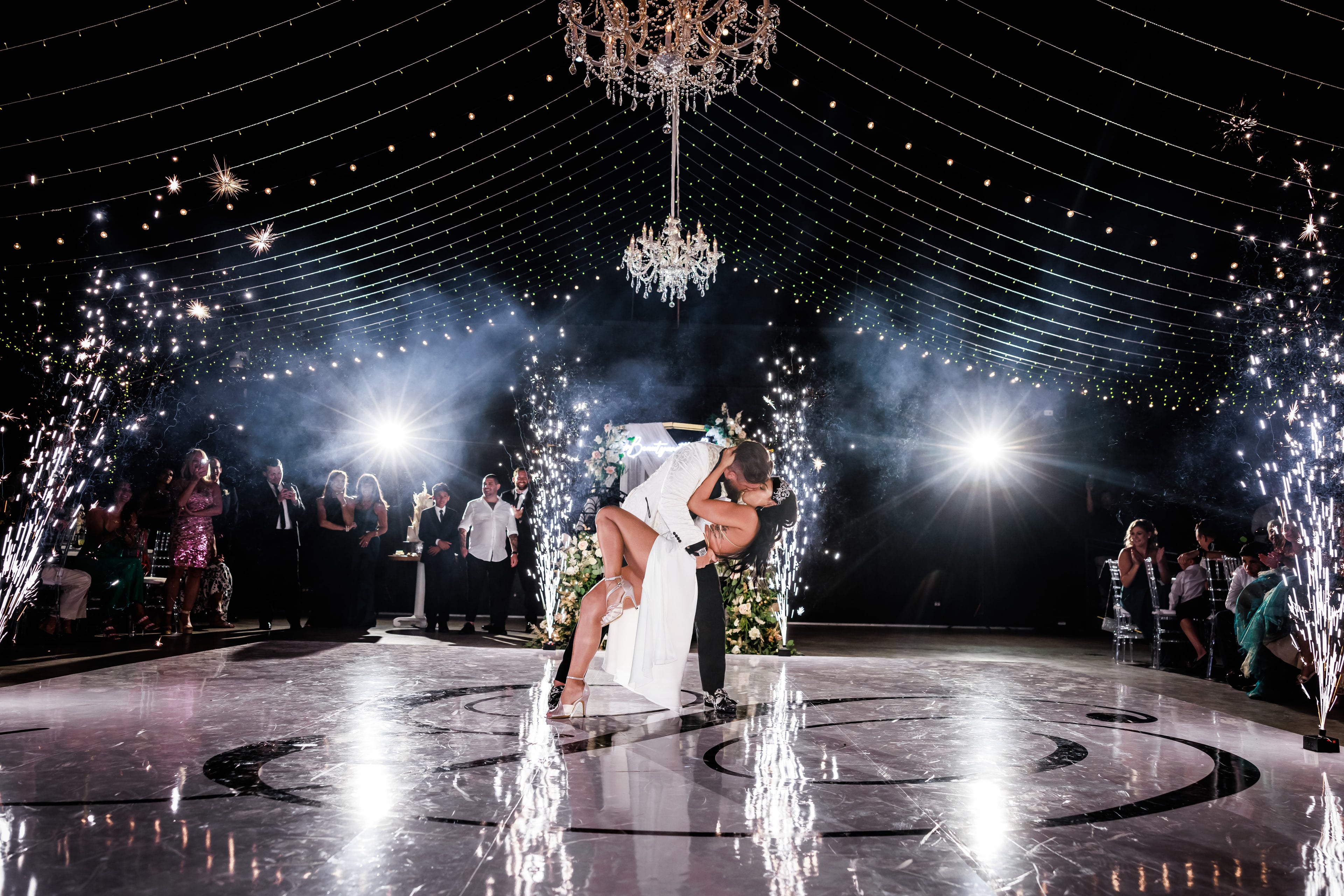Newlyweds dipping beneath chandeliers, fireworks, and reception lights