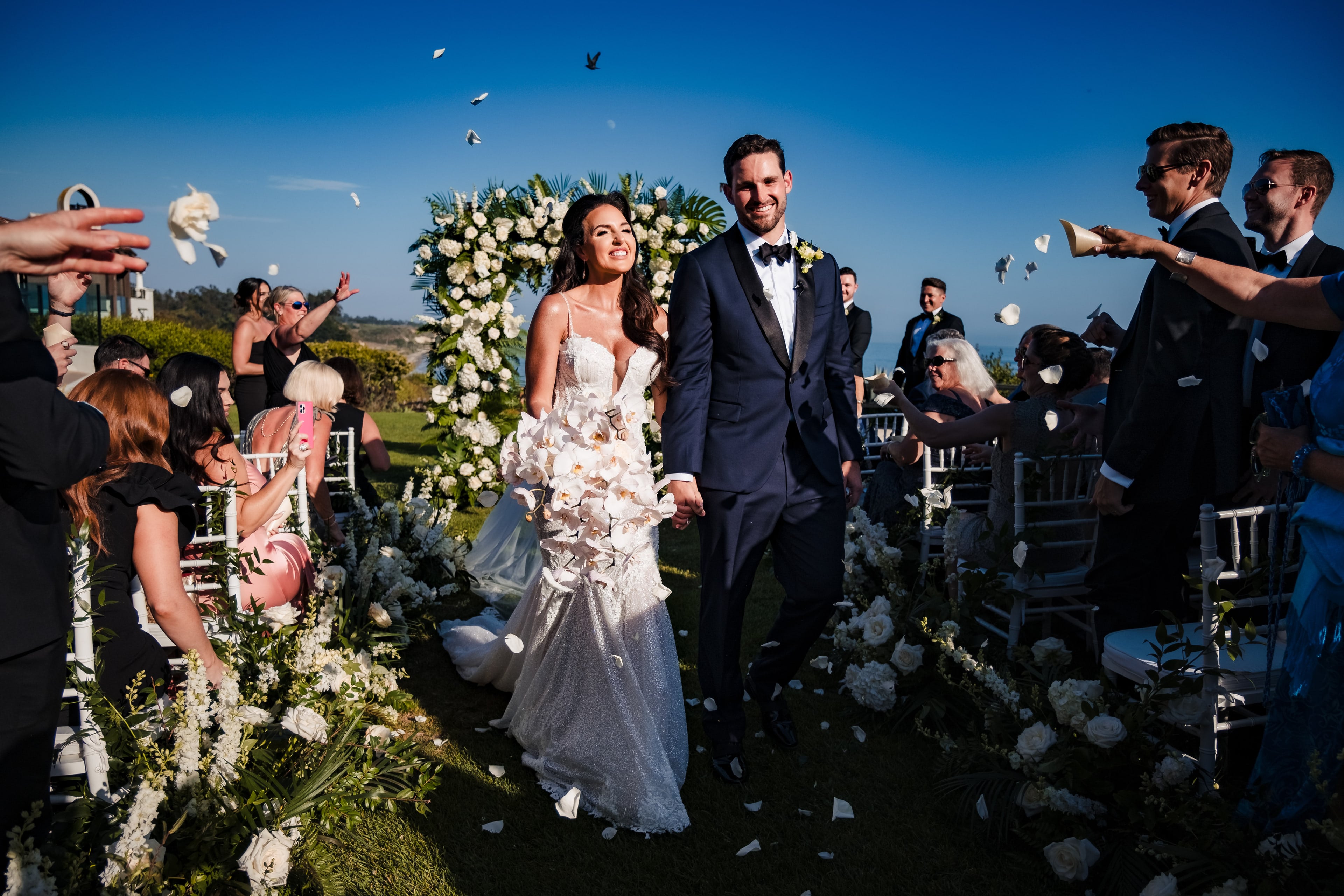Newlyweds walking up the aisle as guests toss white petals