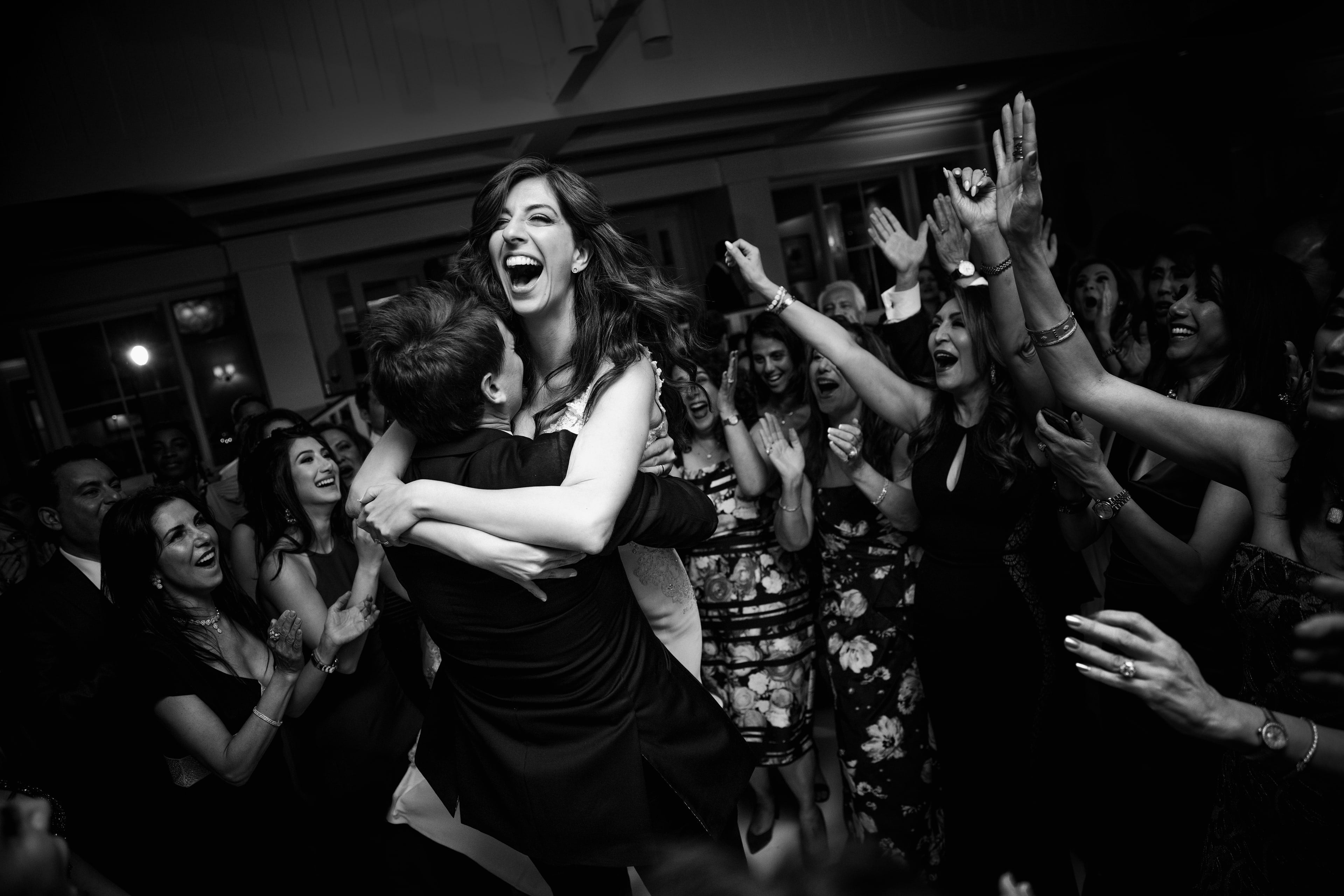 Bride laughing while being lifted on a crowded wedding dance floor