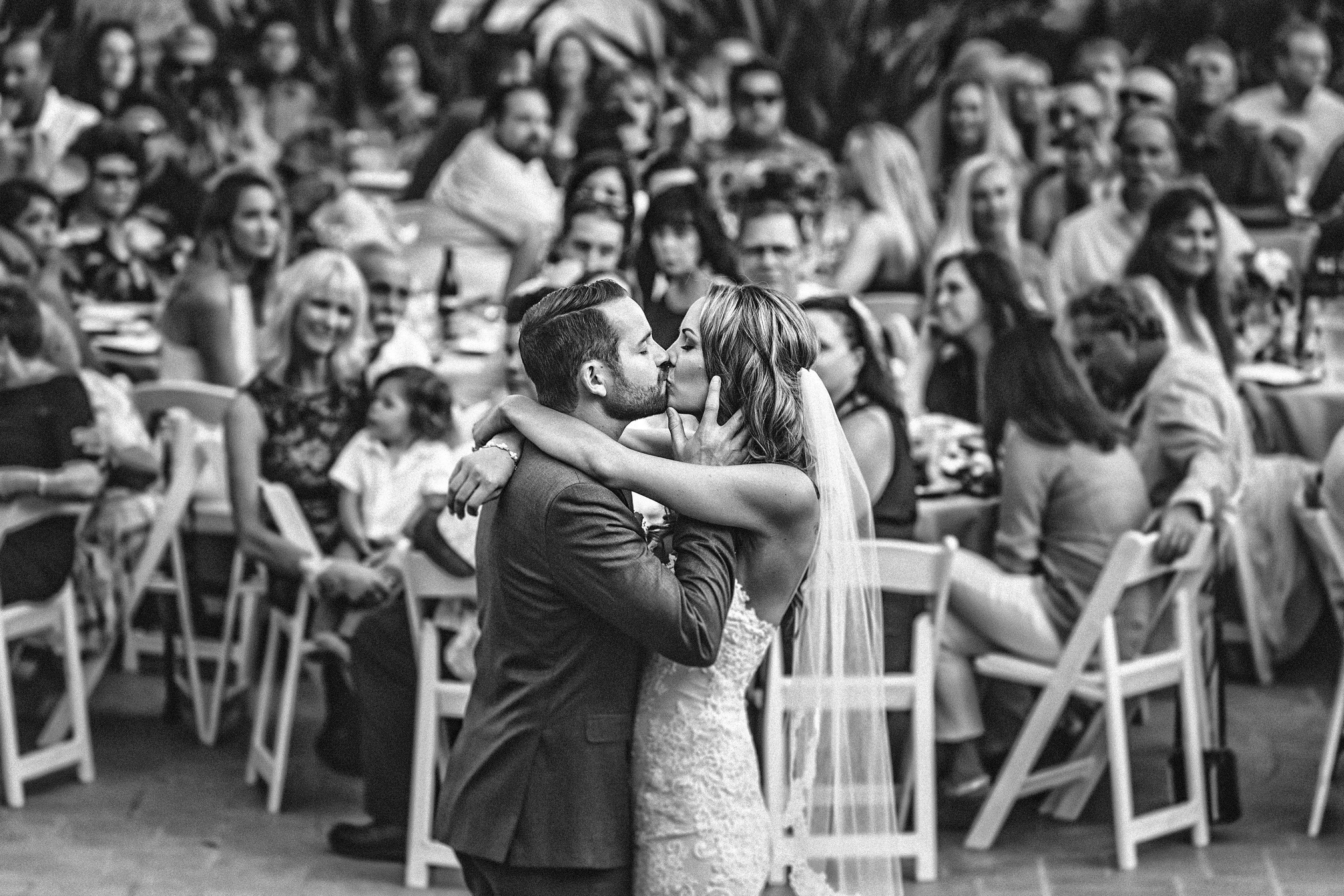 Newlyweds kissing among their guests in a black and white candid moment