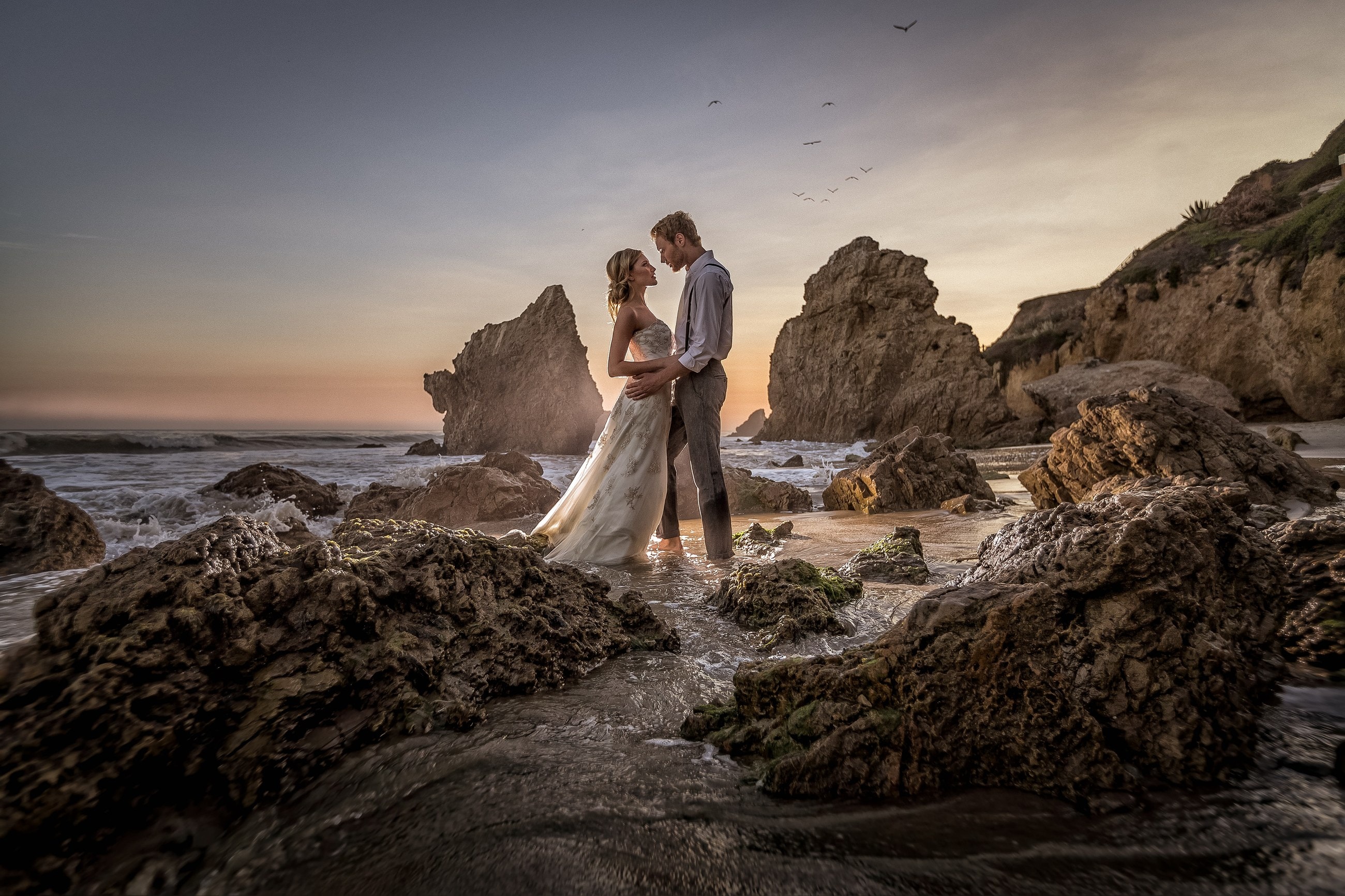 Newlyweds standing among the rocks at El Matador Beach near sunset