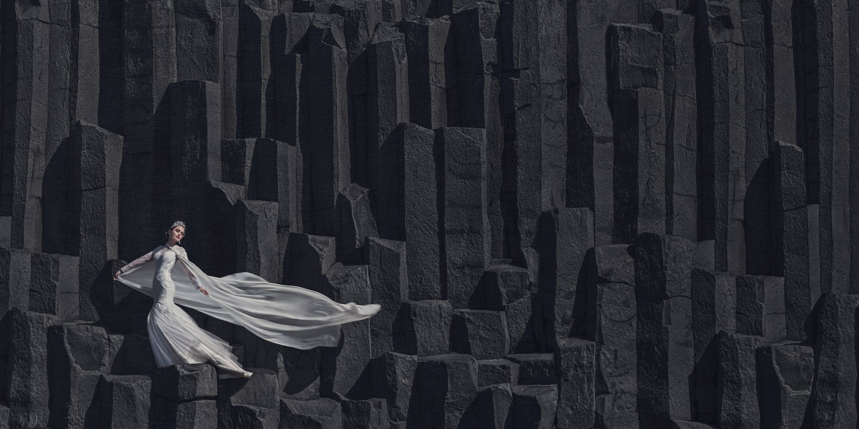 A bride in a flowing gown against Icelandic basalt columns