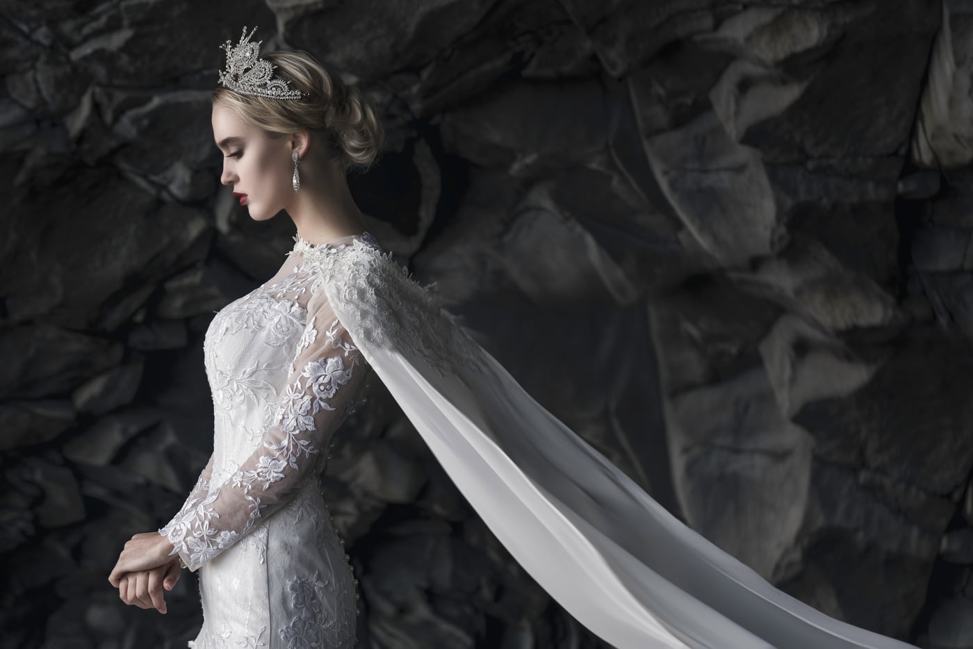 A bride in a lace gown and flowing veil against dark volcanic rock in Iceland