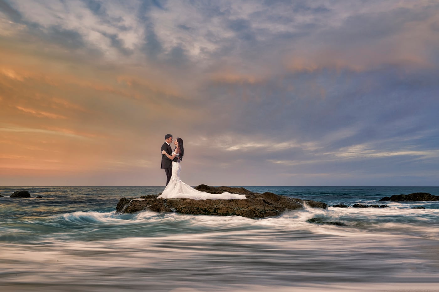 A newly married couple on the rocks beside the ocean at sunset in Cabo San Lucas
