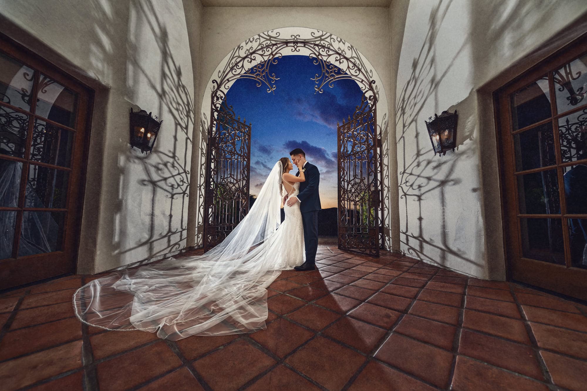 a bride and groom in a Spanish archway with a cathedral veil across the tile, after retouching