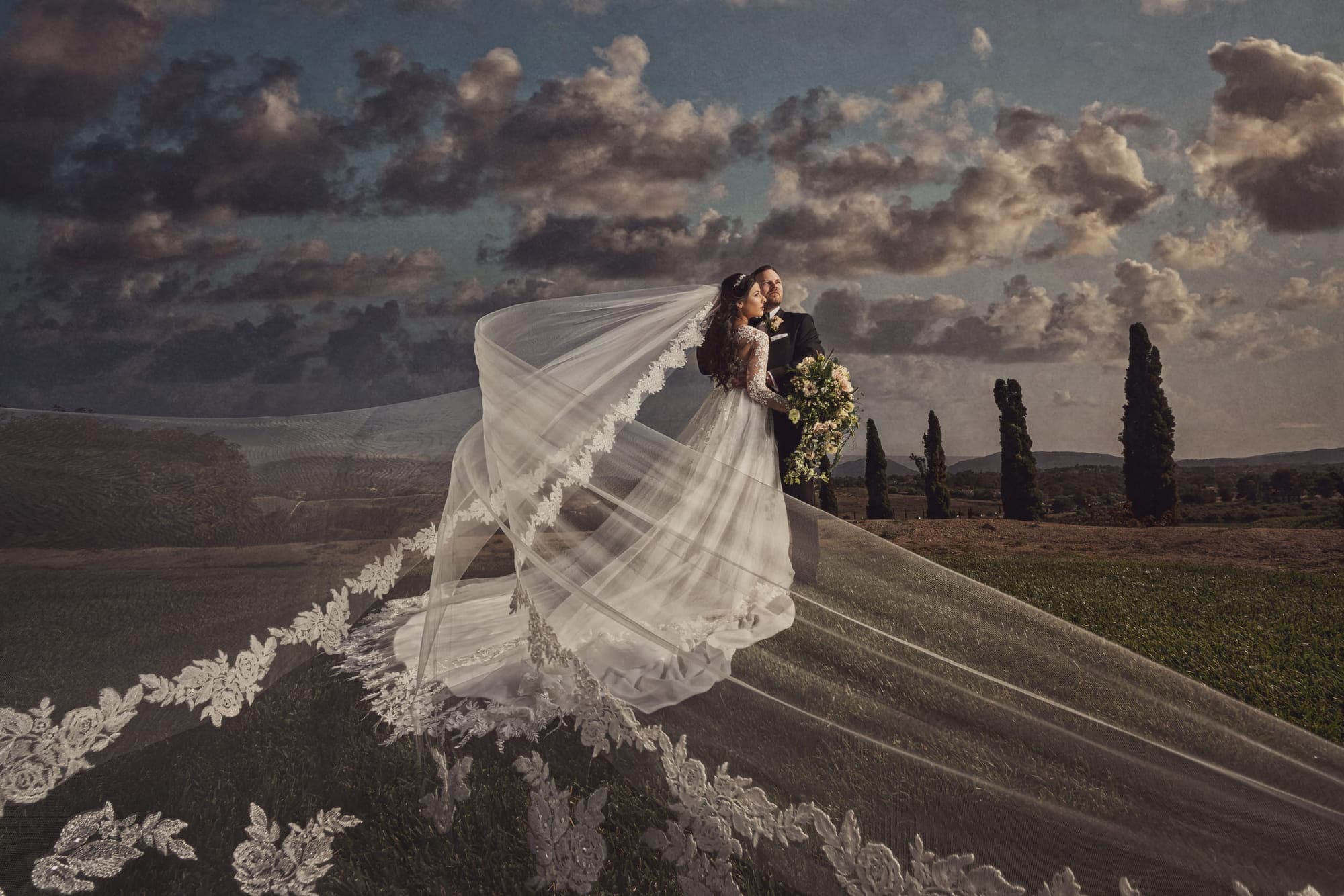 a bride with a cathedral veil sweeping across a Tuscan field, cypress trees behind, after retouching