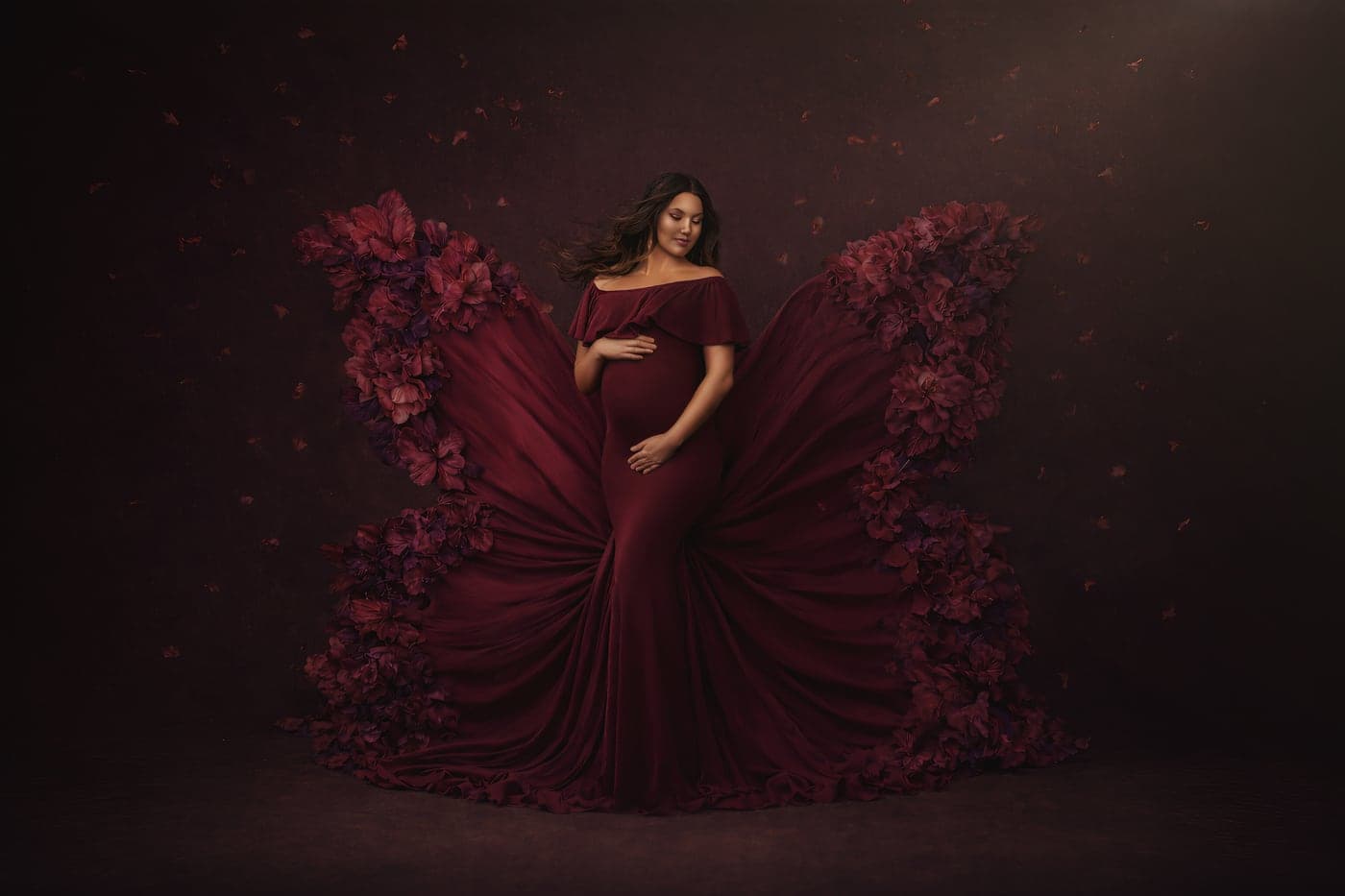 Fine-art maternity portrait in a burgundy gown with a fanned floral train