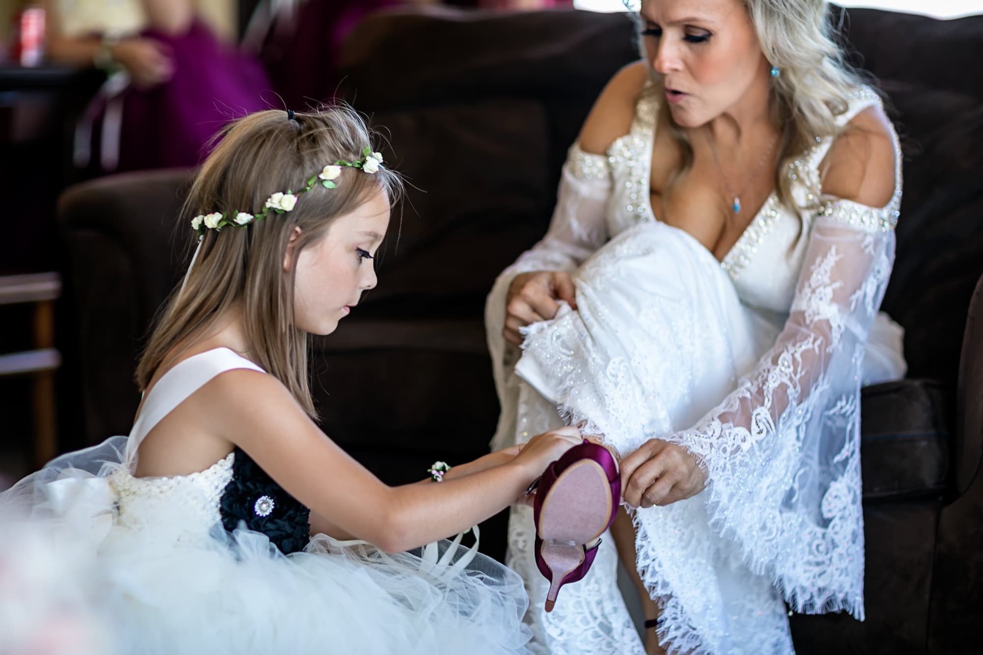 A young attendant in a flower crown carefully helping Sheridi with her shoe before the ceremony