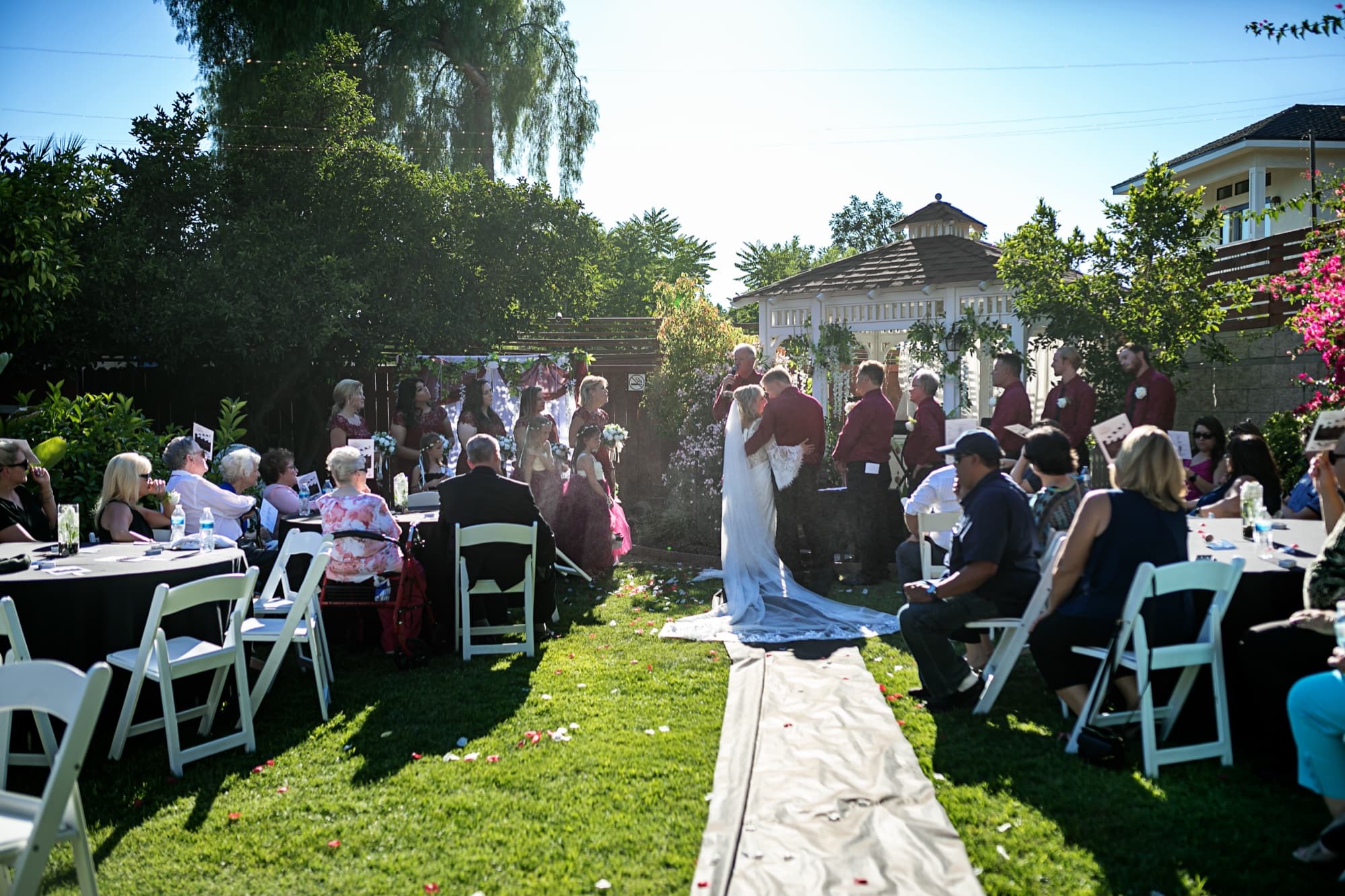 Wide view of the garden ceremony at 40 Palms Estates, Sheridi's long train pouring down the aisle runner in the afternoon sun