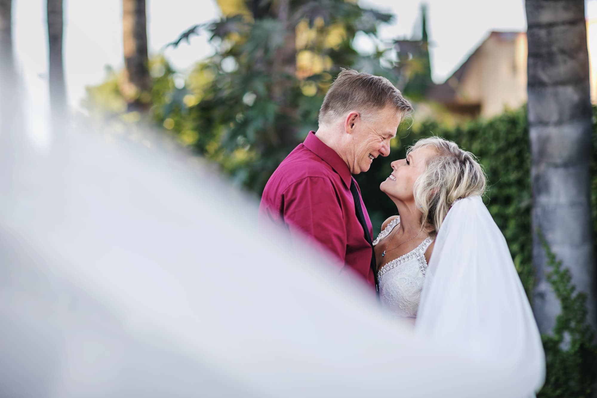Sheridi and Greg kissing framed through her veil in the gardens at 40 Palms Estates