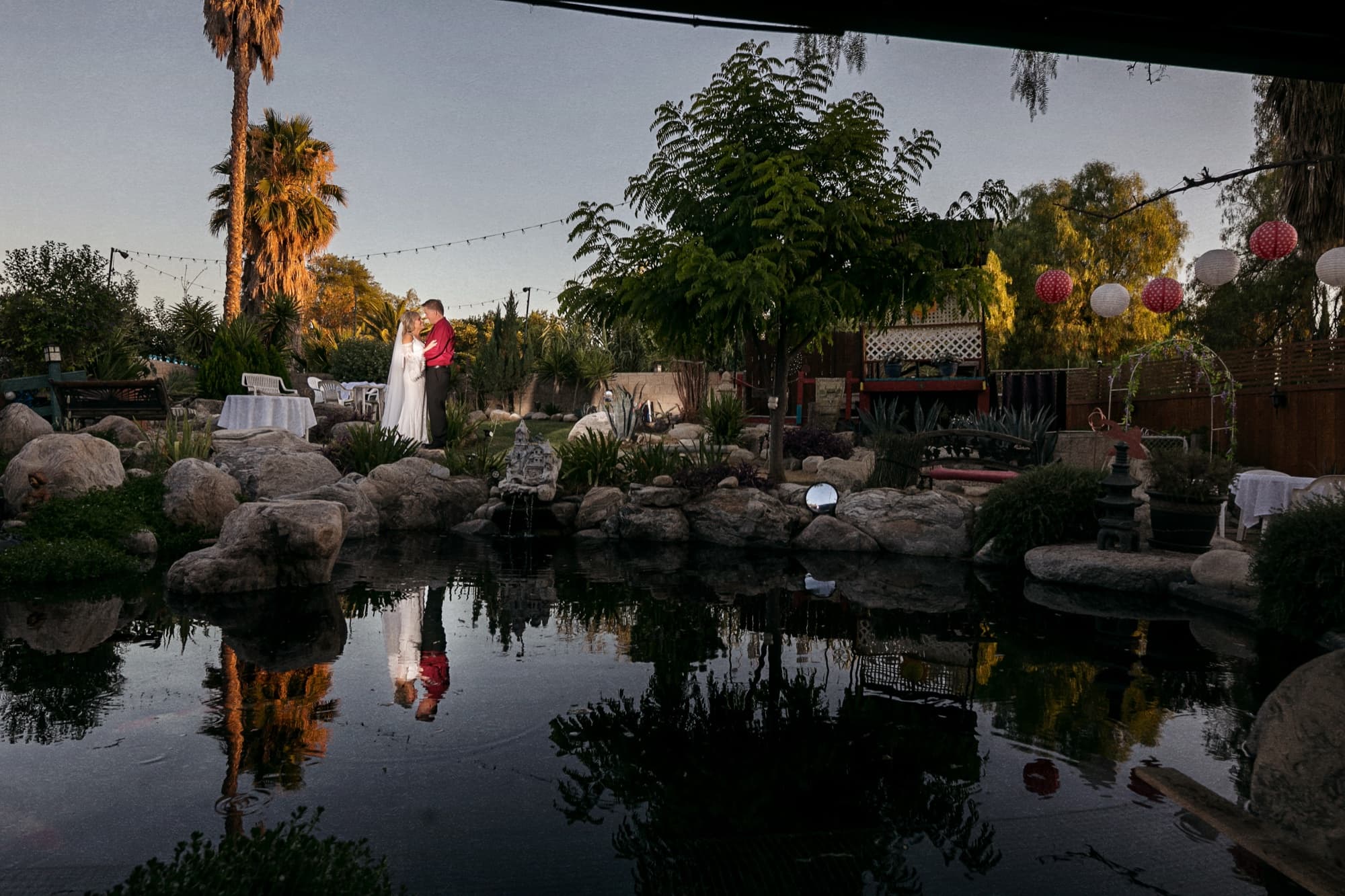 Sheridi and Greg at the edge of the koi pond at sunset, the sky and lanterns reflected in the still water