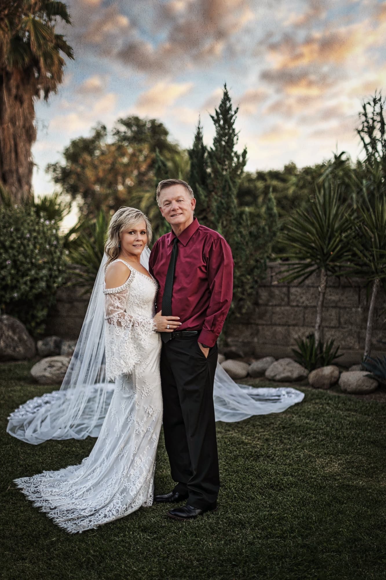 Sheridi and Greg under a dramatic sunset sky, her veil spread across the estate lawn