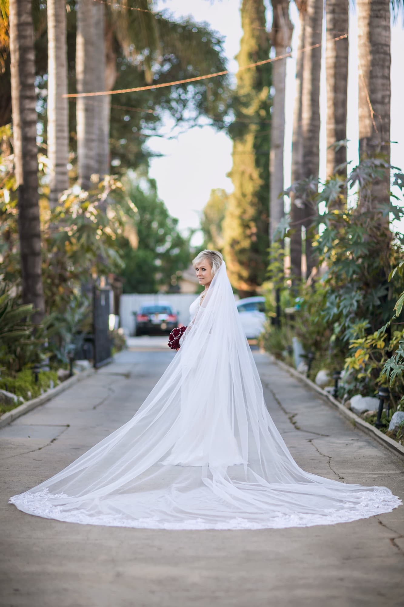 Sheridi standing in the palm-lined corridor at 40 Palms Estates in Reseda, her cathedral veil and train stretched the length of the drive, photographed by Michael Anthony Photography