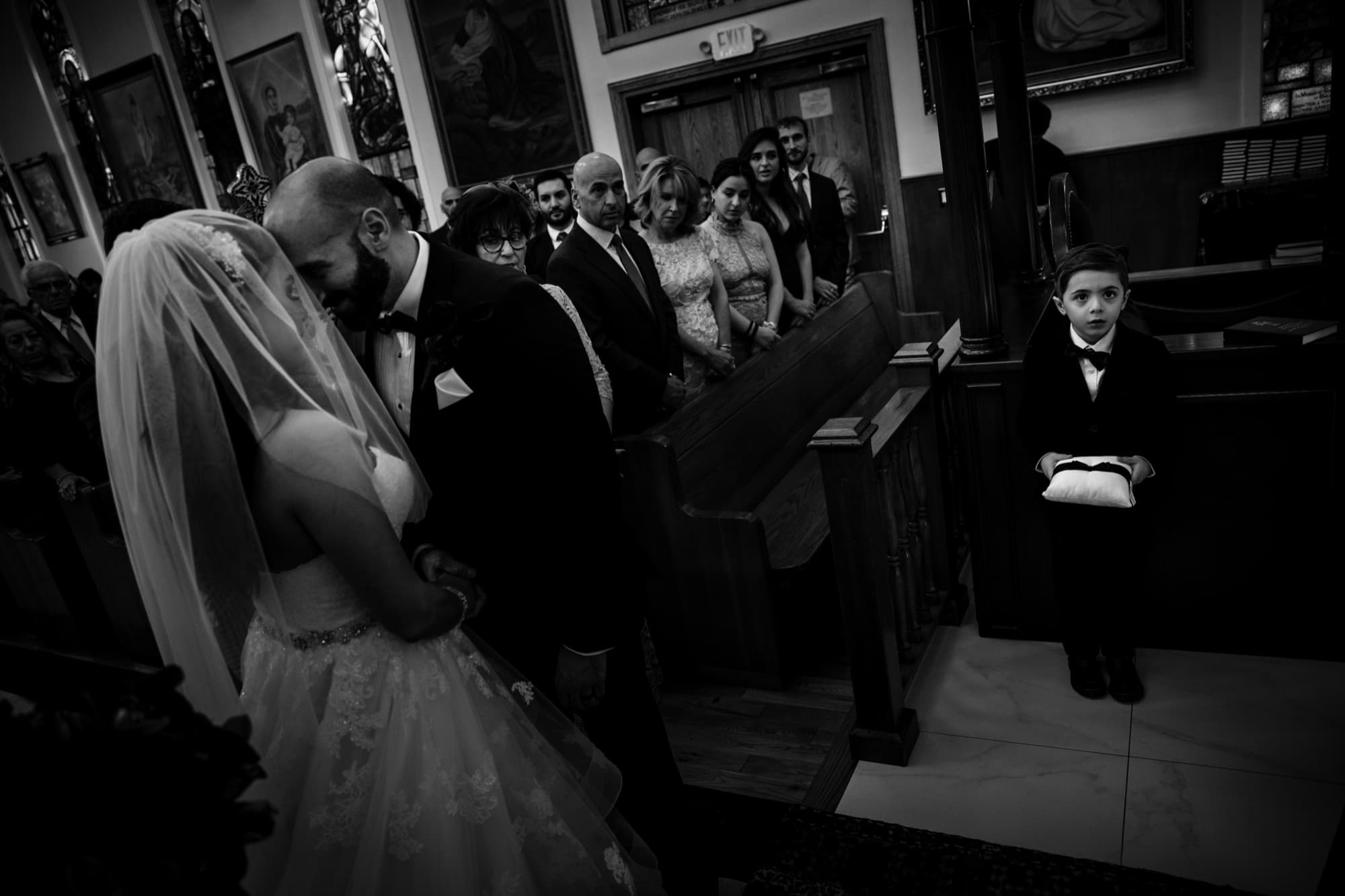 Black and white photograph of Margaret and Hrug bowing together during their Armenian Apostolic ceremony as a young ring bearer watches