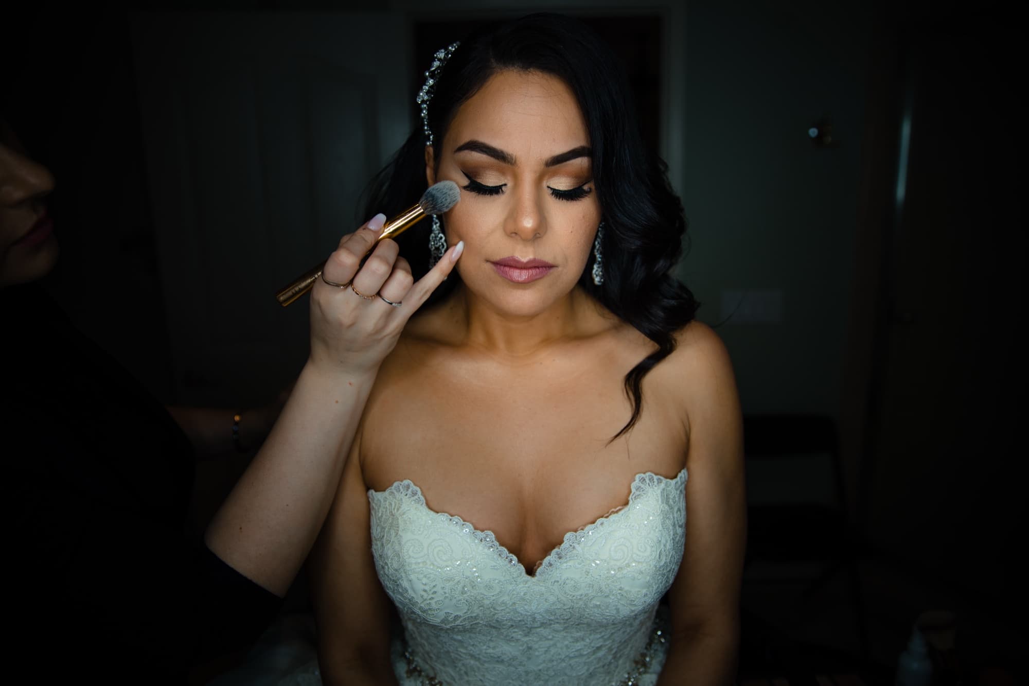 Margaret in a mint beaded gown having her makeup finished with a brush during getting-ready