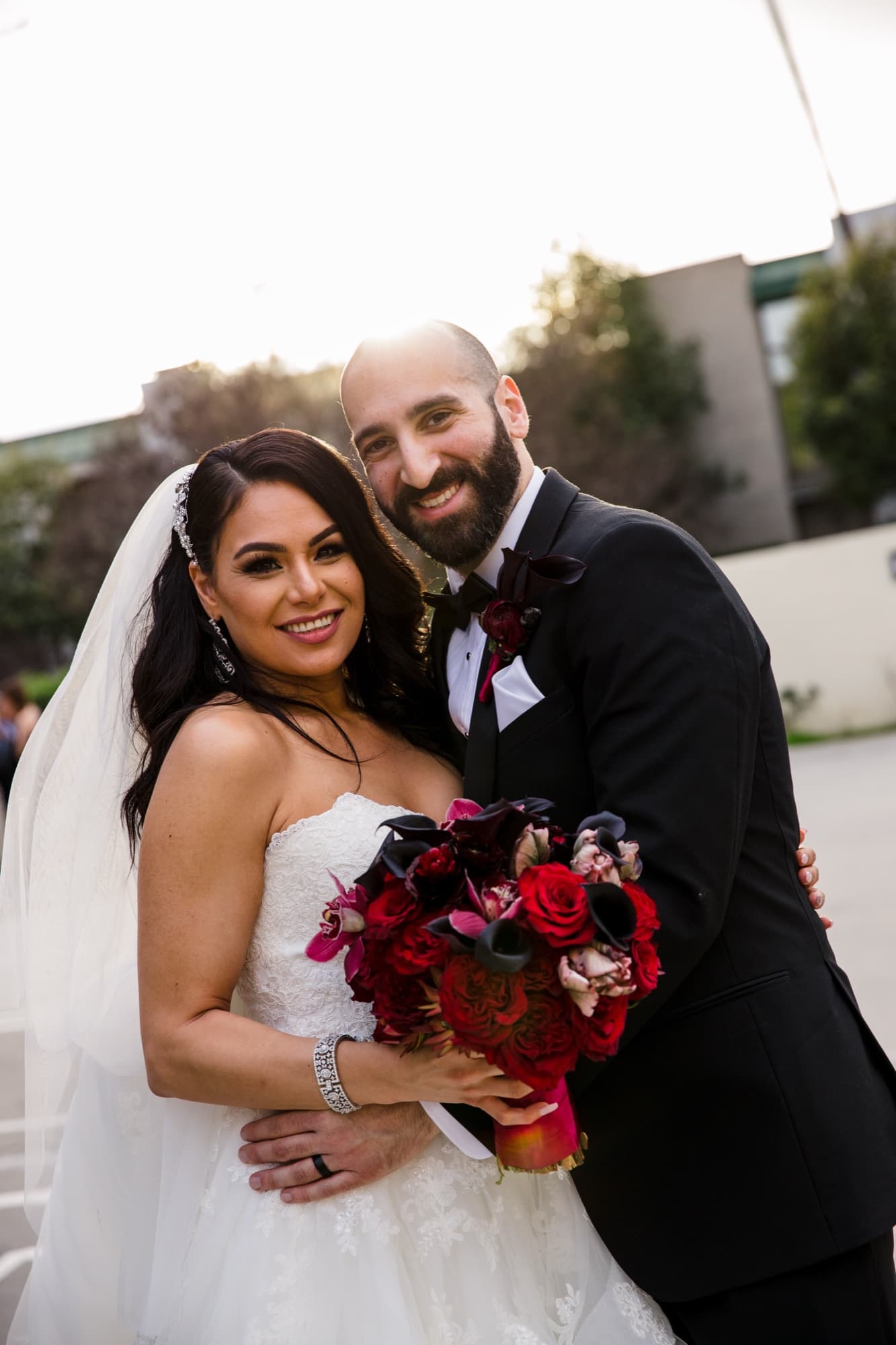 Margaret and Hrug smiling together outdoors, her deep-red rose bouquet held between them
