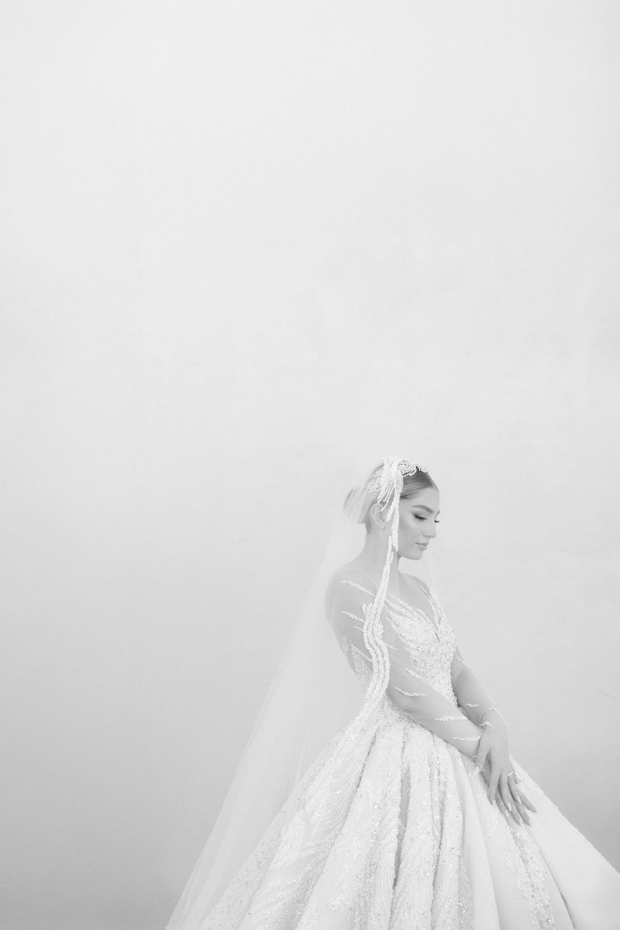 High-key bridal portrait of the bride in her beaded gown and cathedral veil against a pale wall