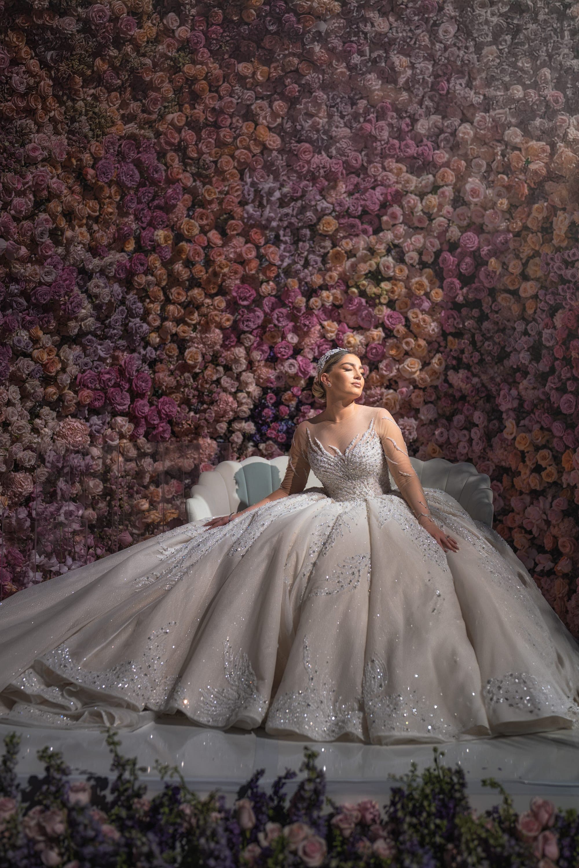 The bride in her full ballgown and cathedral veil against a deep pink and lavender rose wall