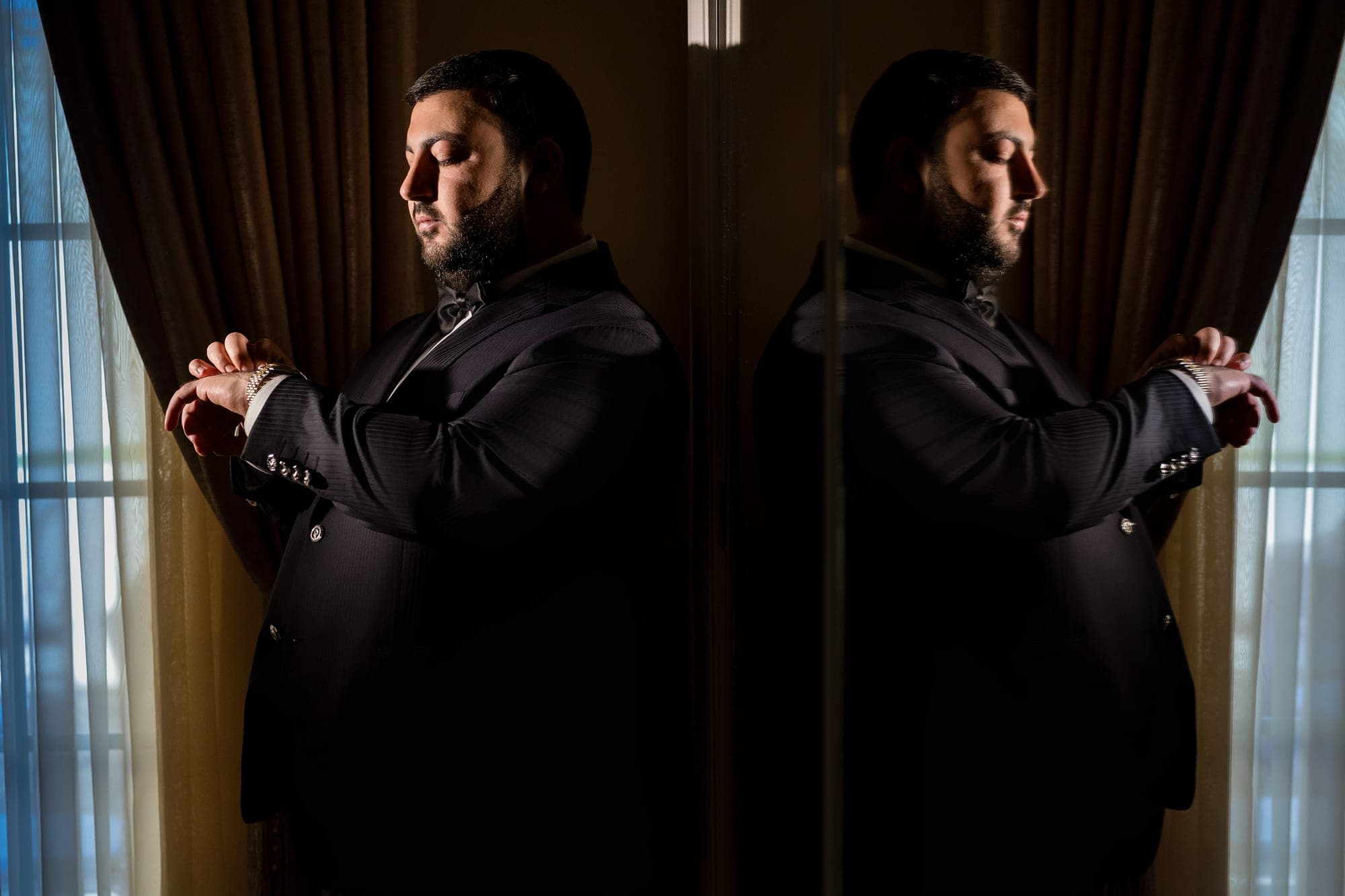 Vardan fastening his cuff in a black tuxedo, reflected in a mirror