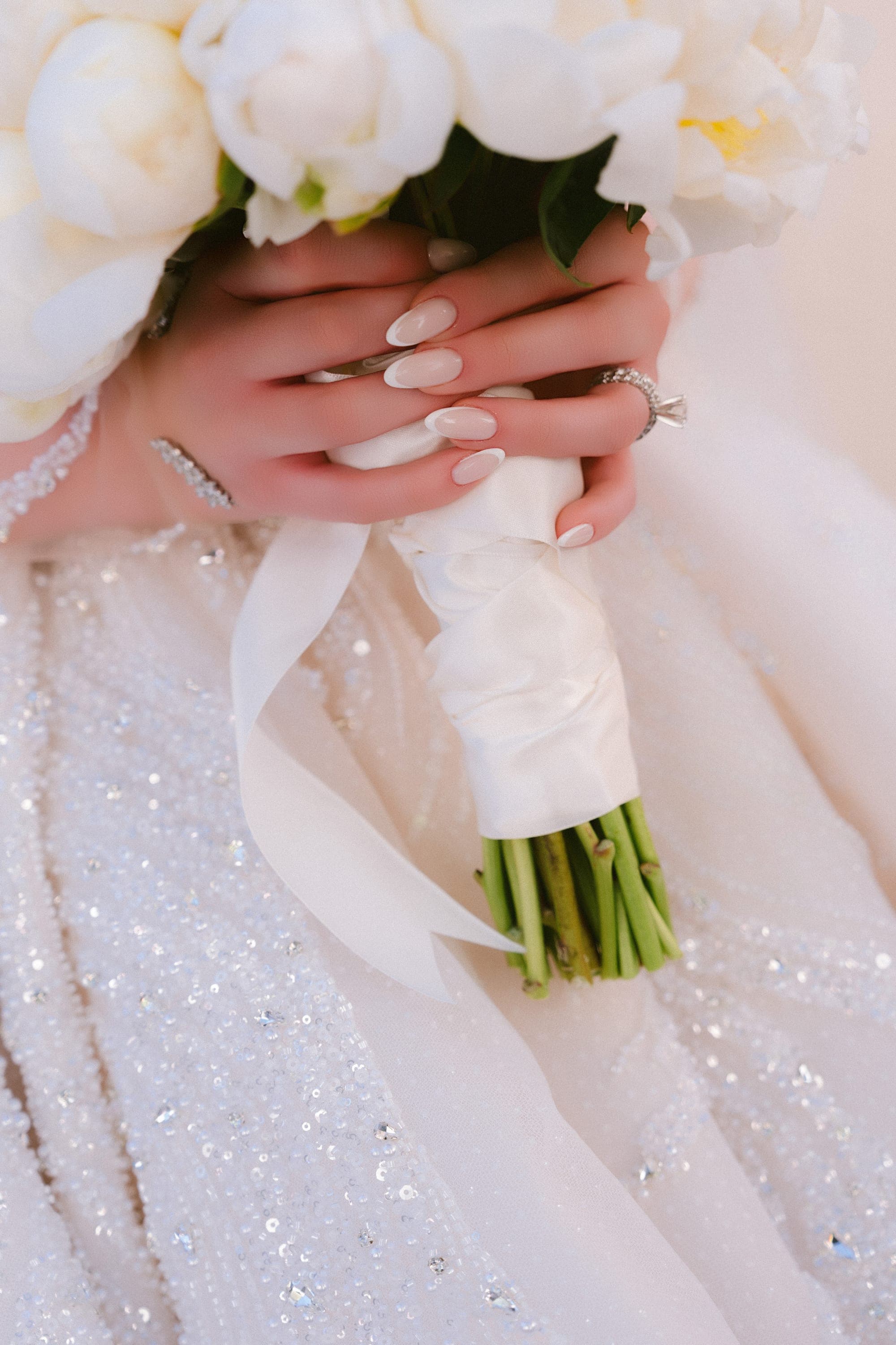 The bride holding a bouquet of white peonies against her beaded gown