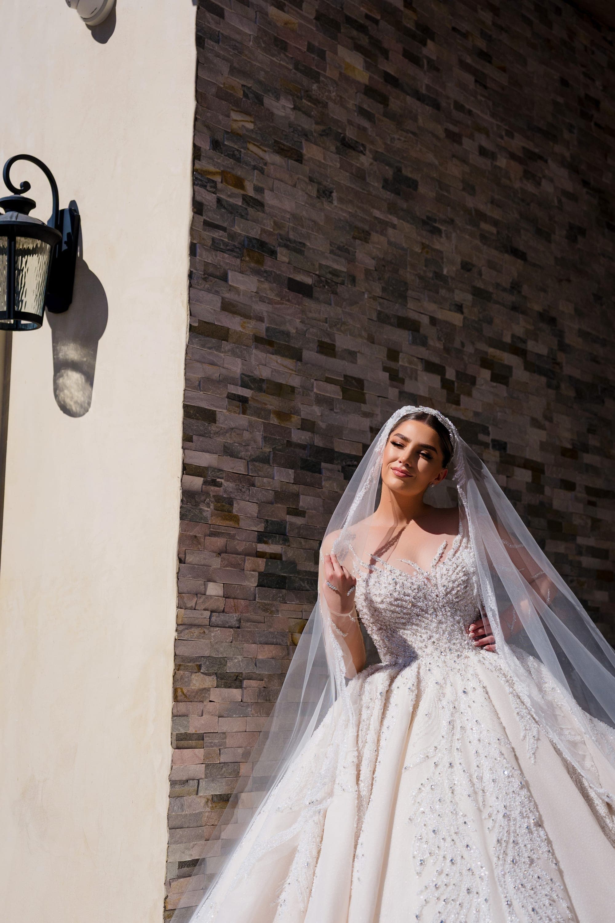 The bride in her ballgown and veil against a stone wall