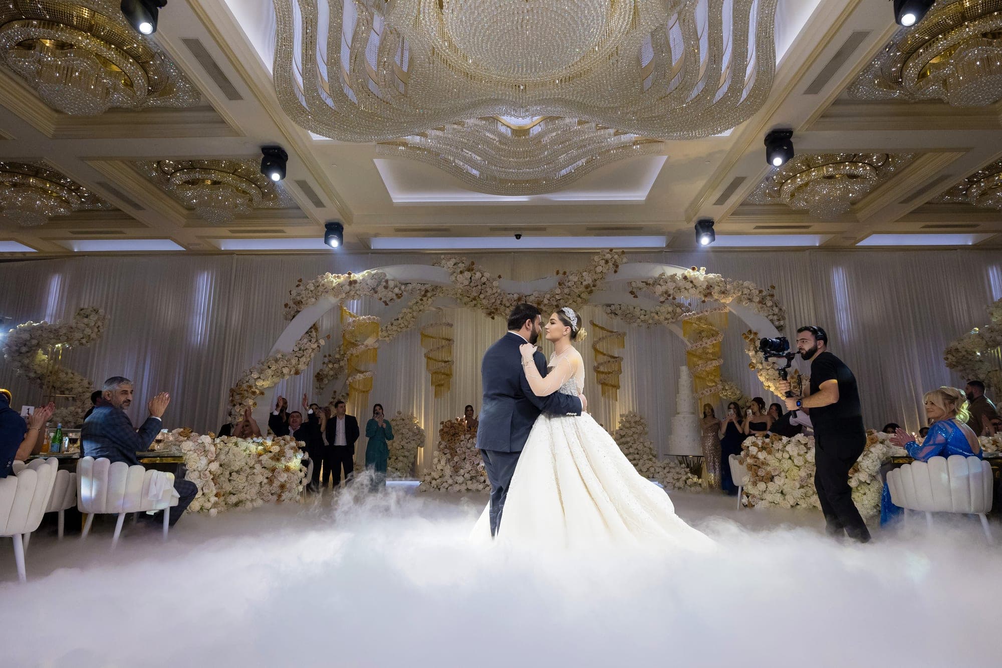 The bride and groom dancing on a low cloud of fog beneath the ballroom's crystal chandelier