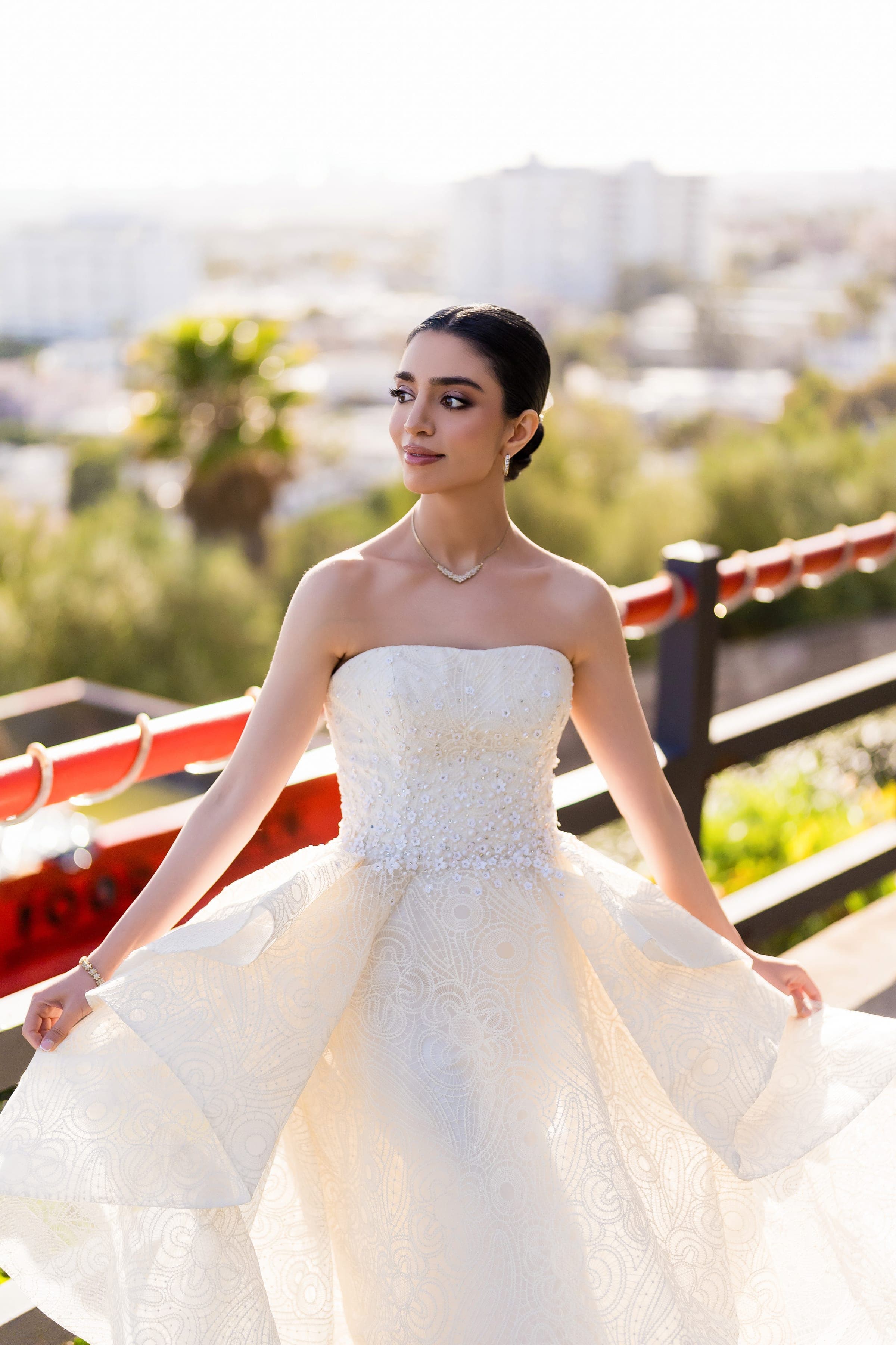 The bride fans out the tiered skirt of her strapless gown in golden light above the city.