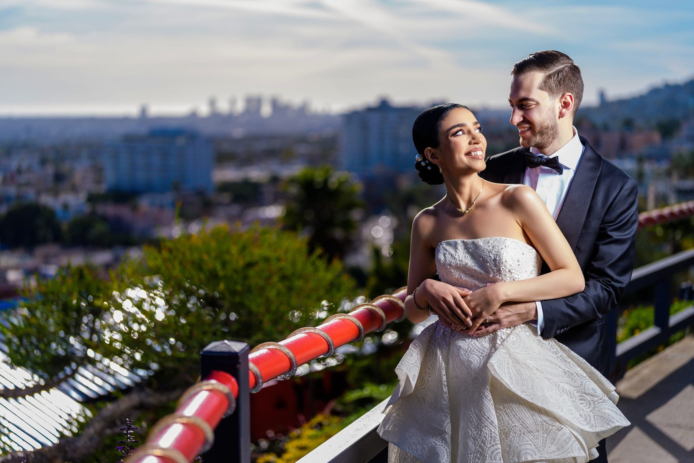The groom hugs the bride from behind as she smiles up at him above the city.